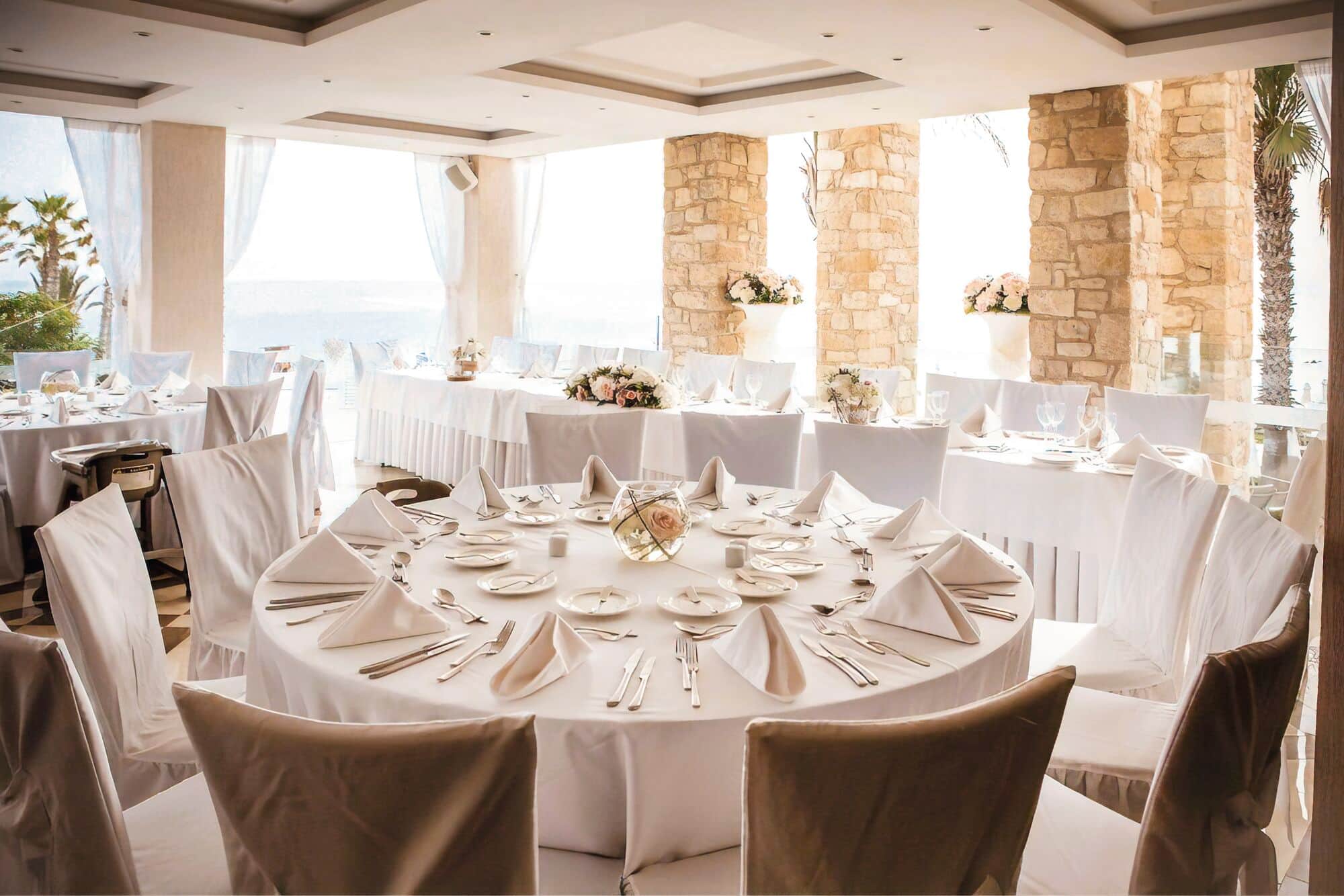 White covered chairs surround round tables dressed for a wedding dinner.