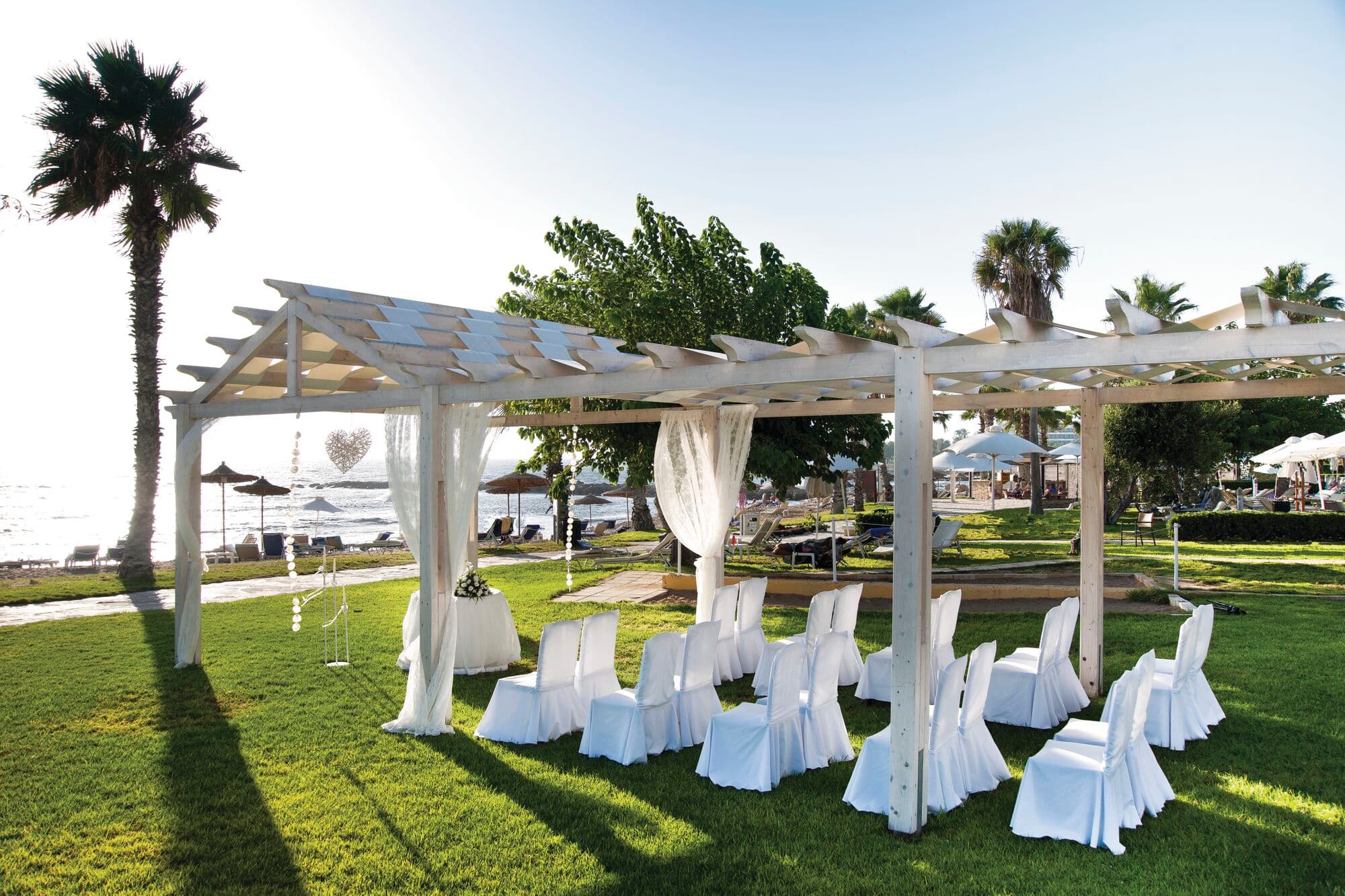 Rows of white chairs face a sandy beach from a grassy lawn. A white gazebo covers the wedding ceremony space.