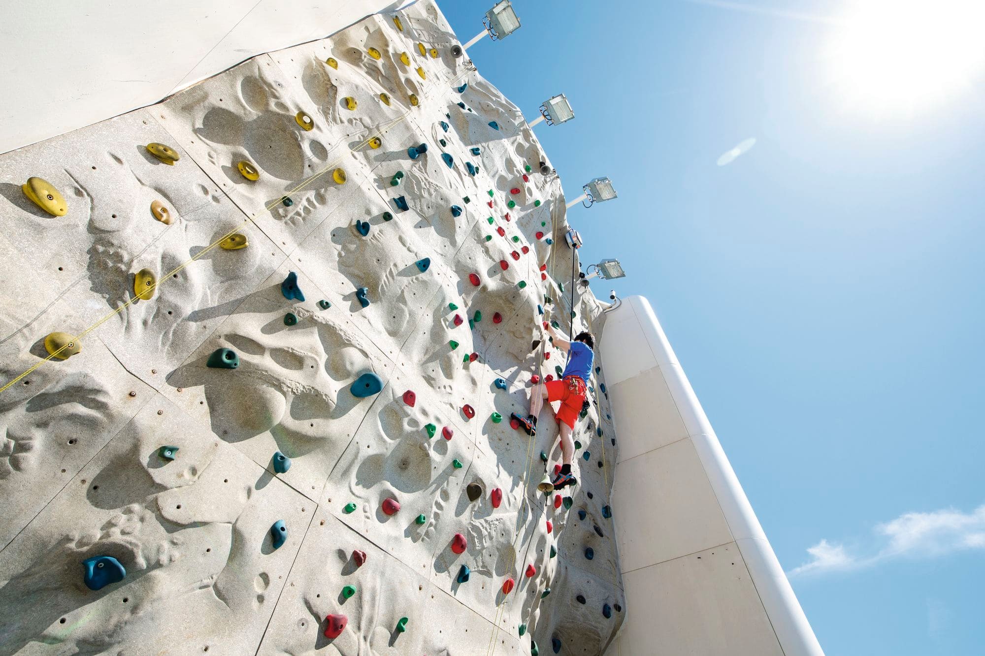 A view below a boy climbing a wall with coloured grips.