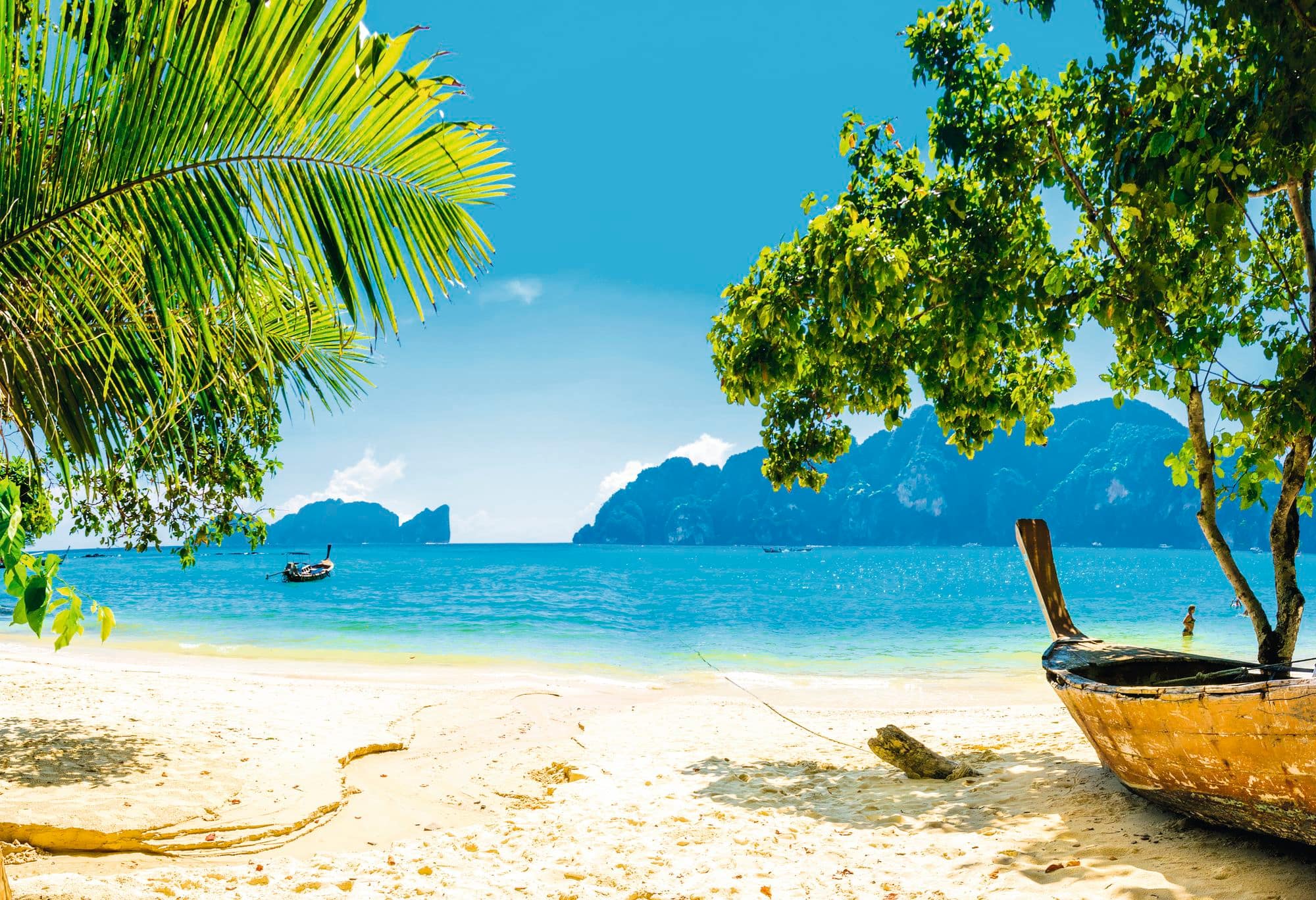 A tropical beach with turquoise water, limestone islands, and traditional longtail boat. 