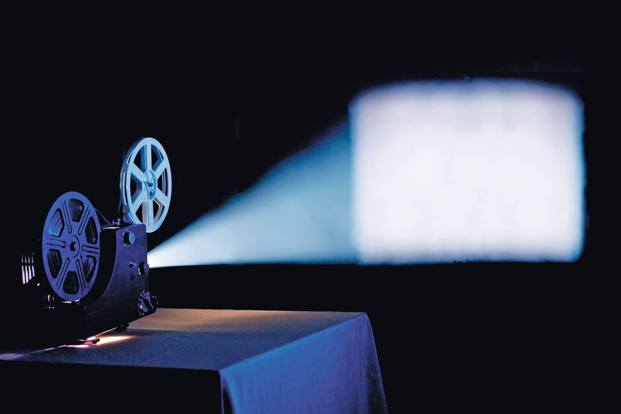 Vintage film projector displaying a movie in a dark room.