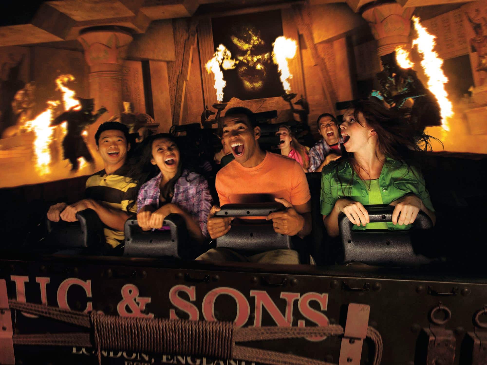 Guests scream on a ride with indoor temple vibes as fire erupts around them.