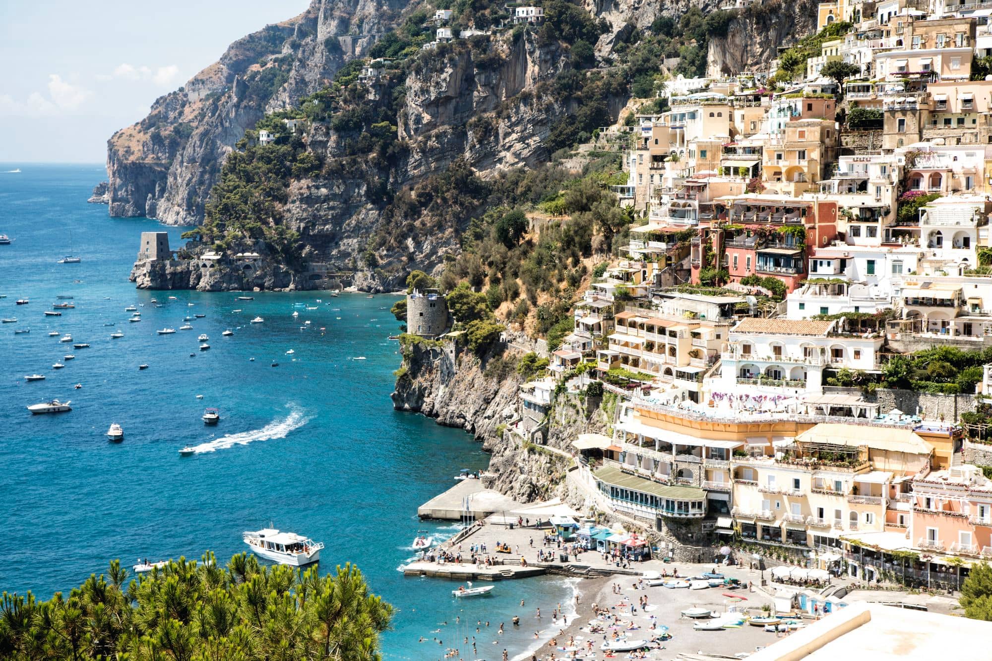 The cliffside village of Positano surrounded by small boats in turquoise seas.