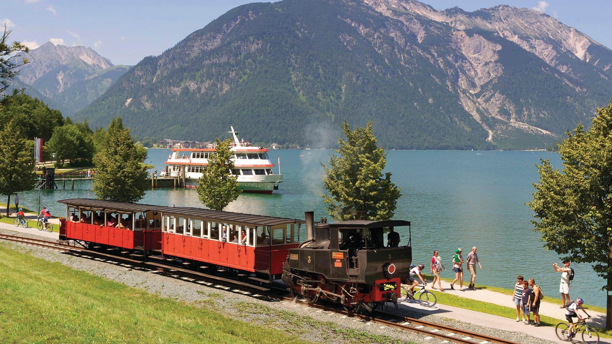 A vintage red steam train next to a lake in Austria. 