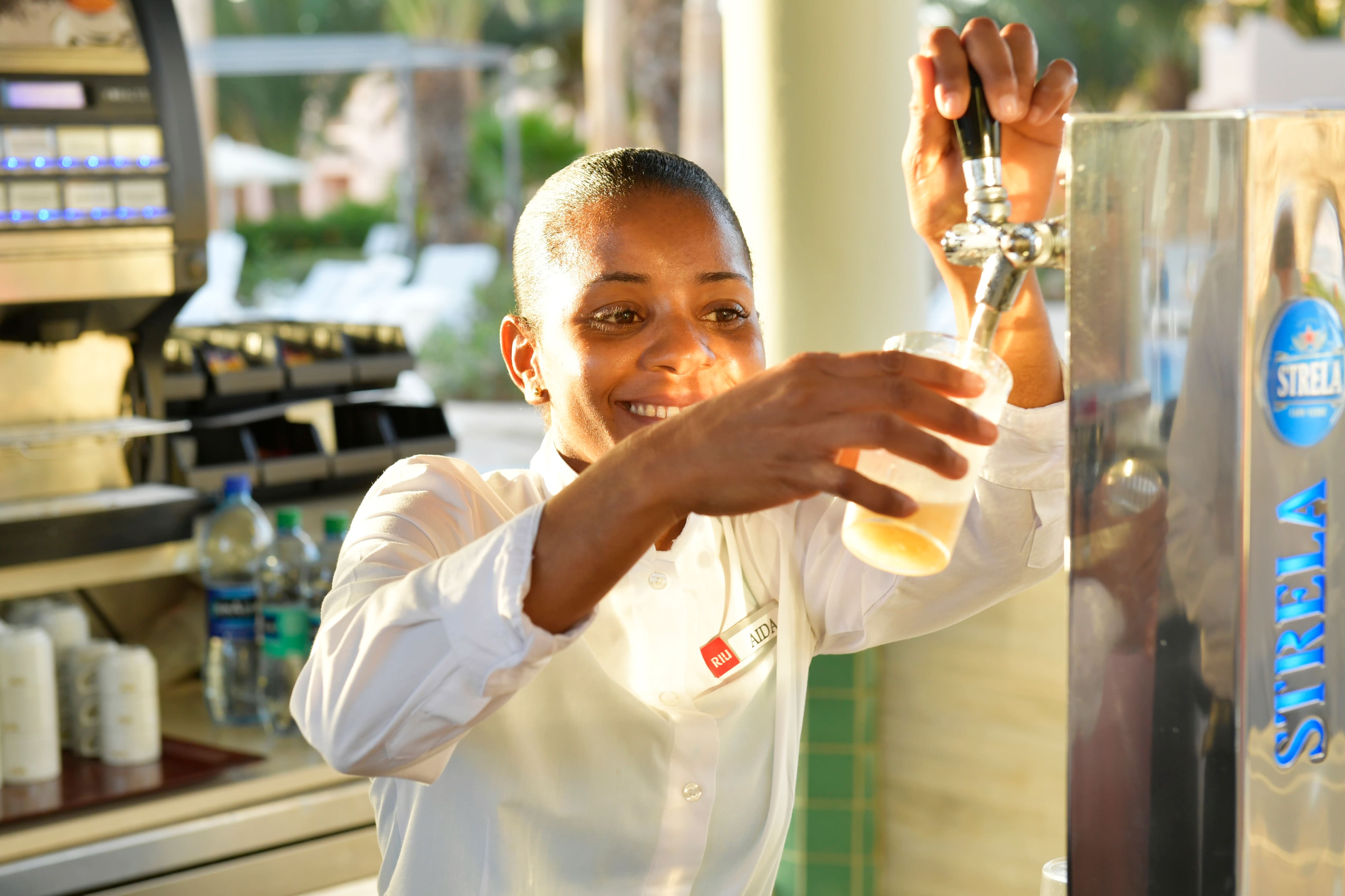 Smiling hospitality worker in white chef's coat pouring a beverage,