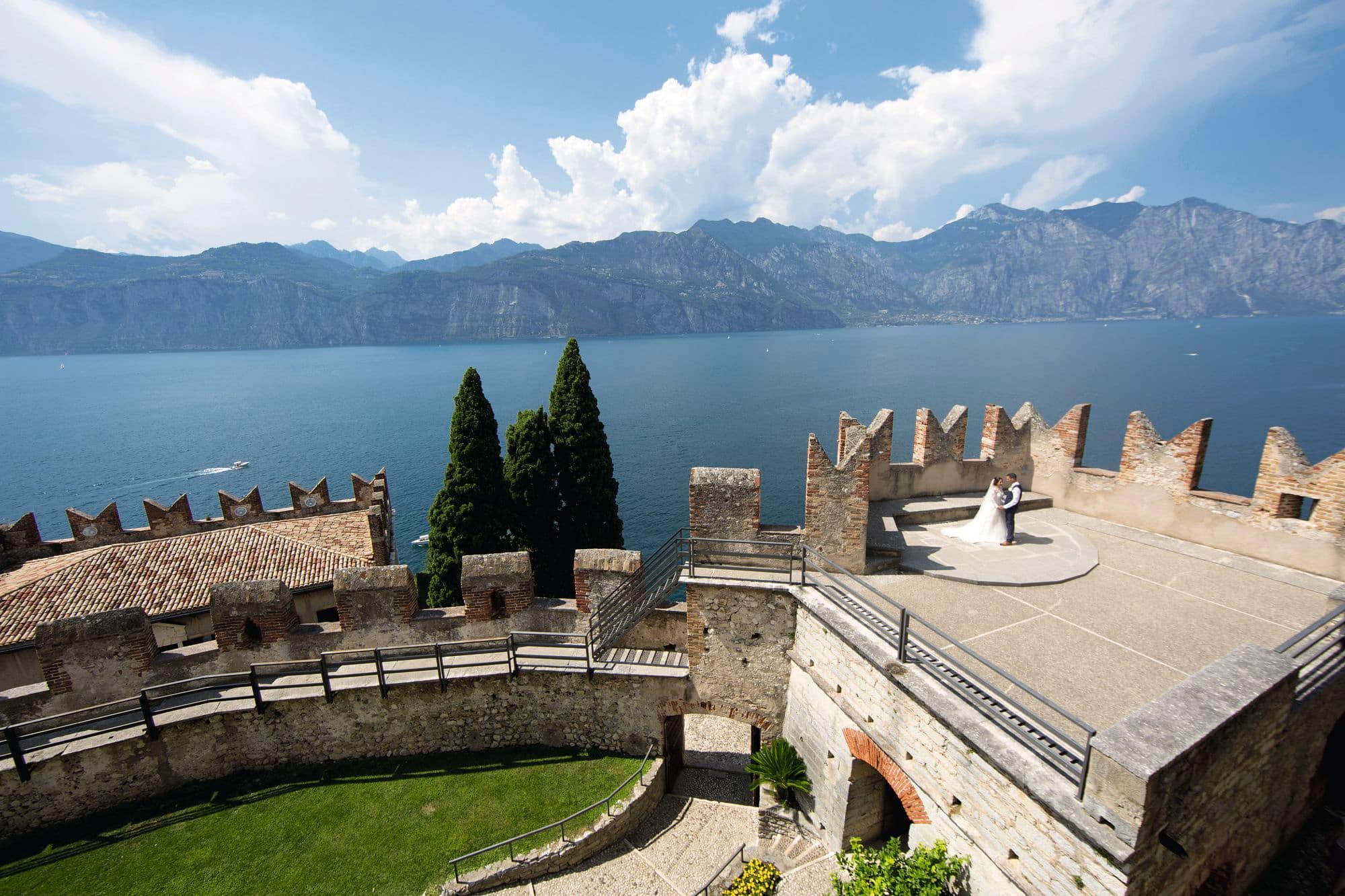 A bride and groom stand on a castle turret overlooking Lake Garda.