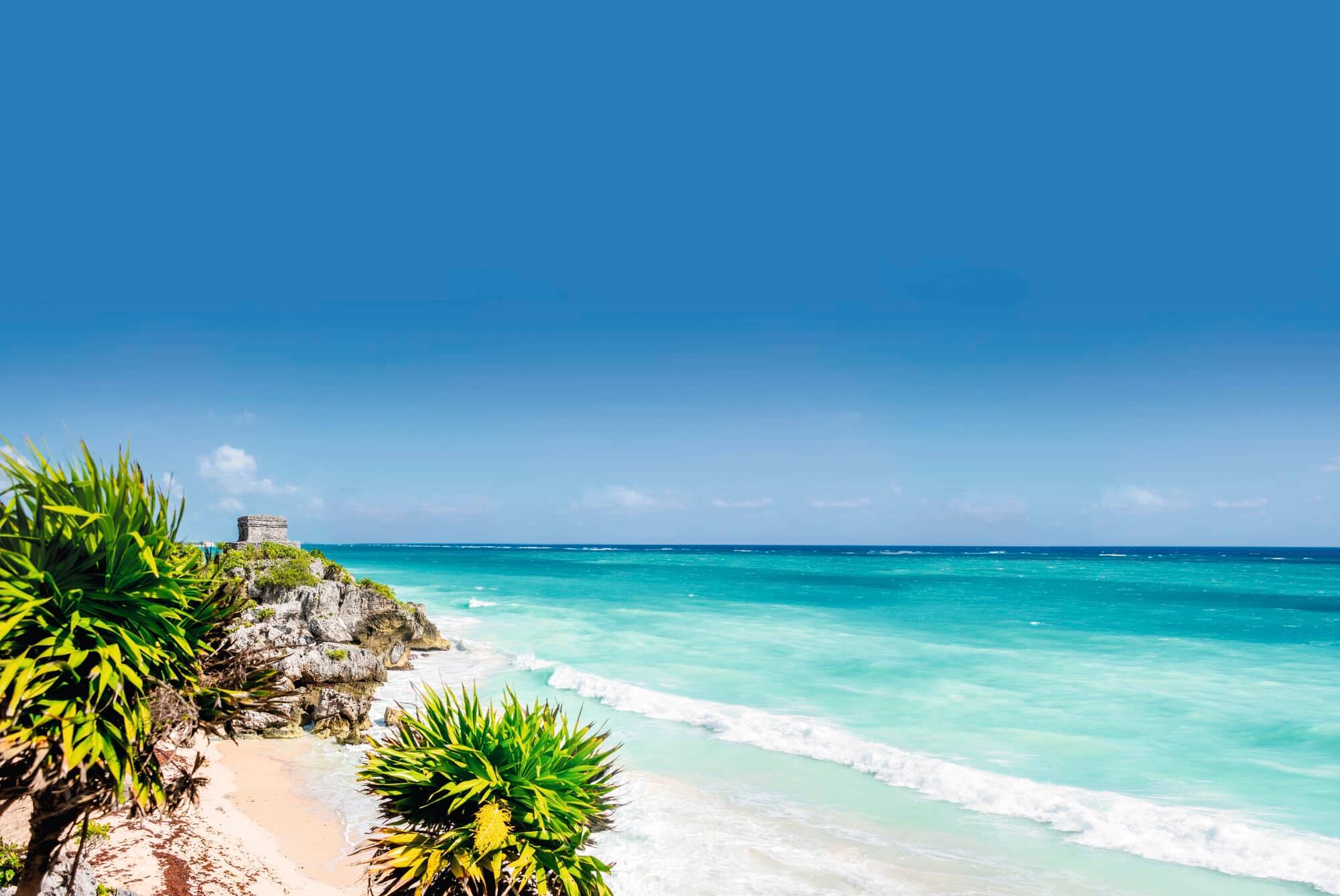 A view of a stone structure on a cliff, overlooking a beach in Mexico.