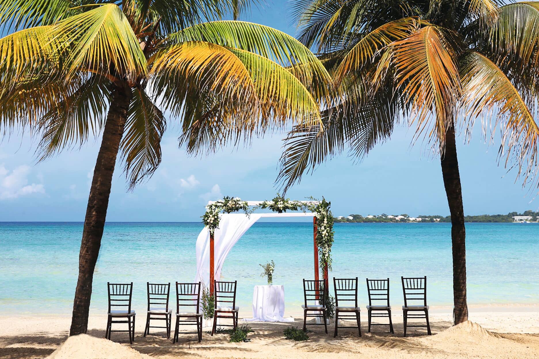 An intimate beach wedding ceremony set-up with a floral arch framed by two great palm trees.