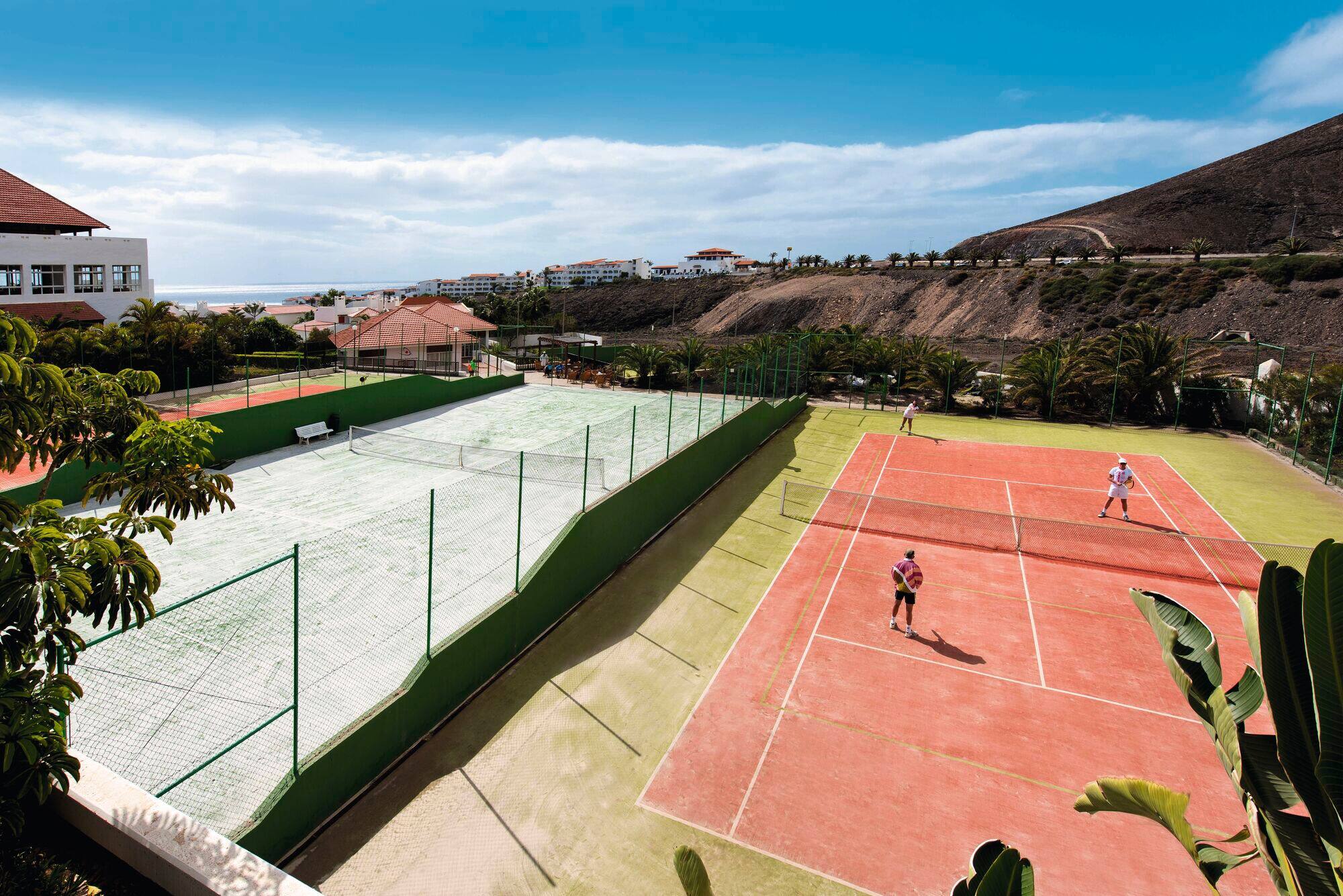 People playing tennis on a court with a view of the surrounding mountainside.