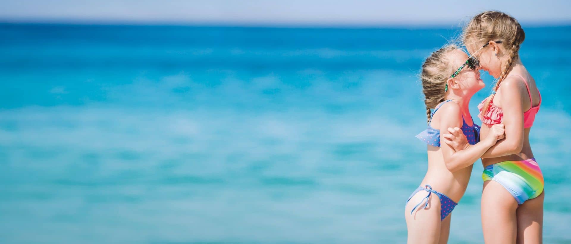 Little girls on a beach looking at each other smiling.