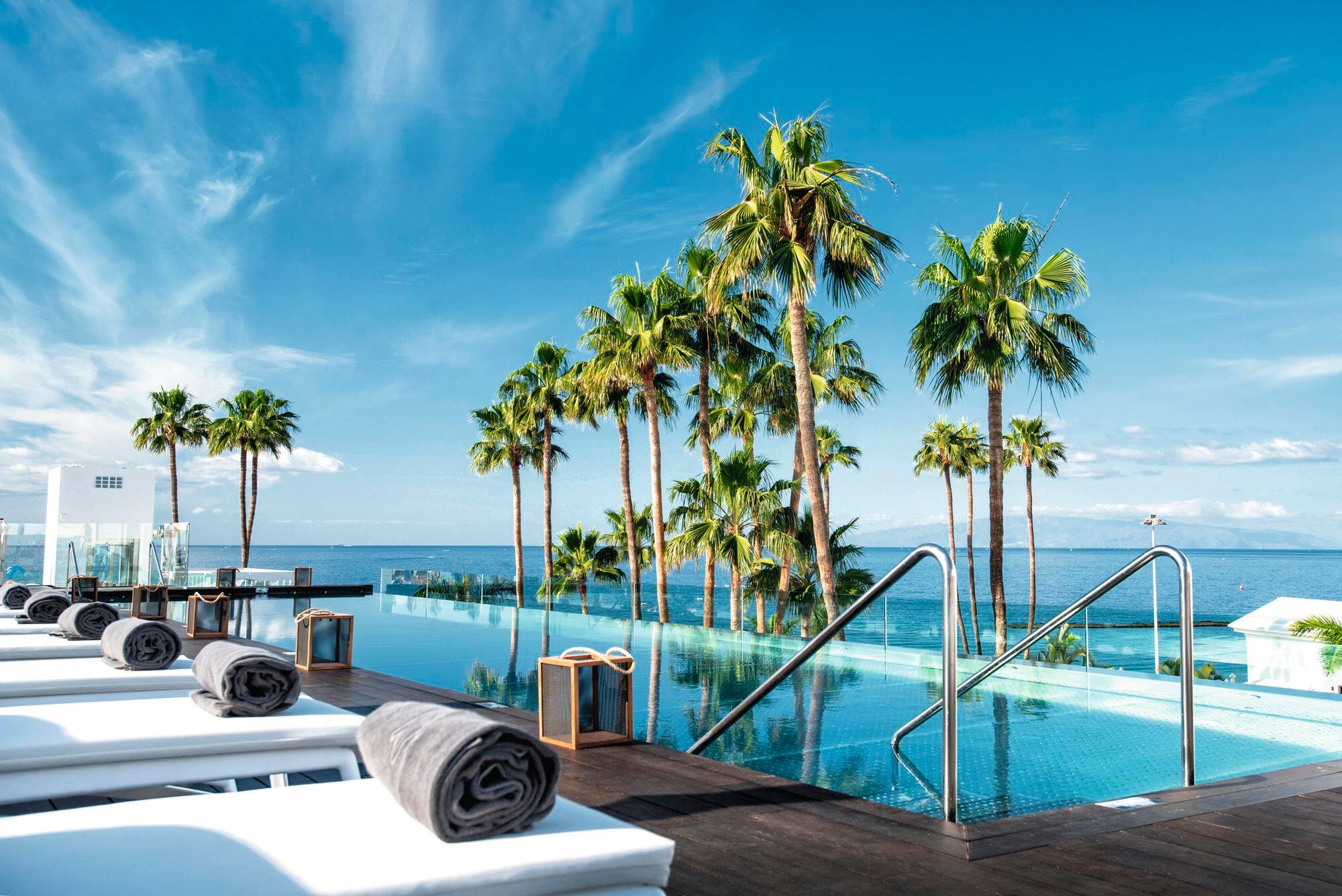 An infinity pool surrounded by palm trees and sun loungers.