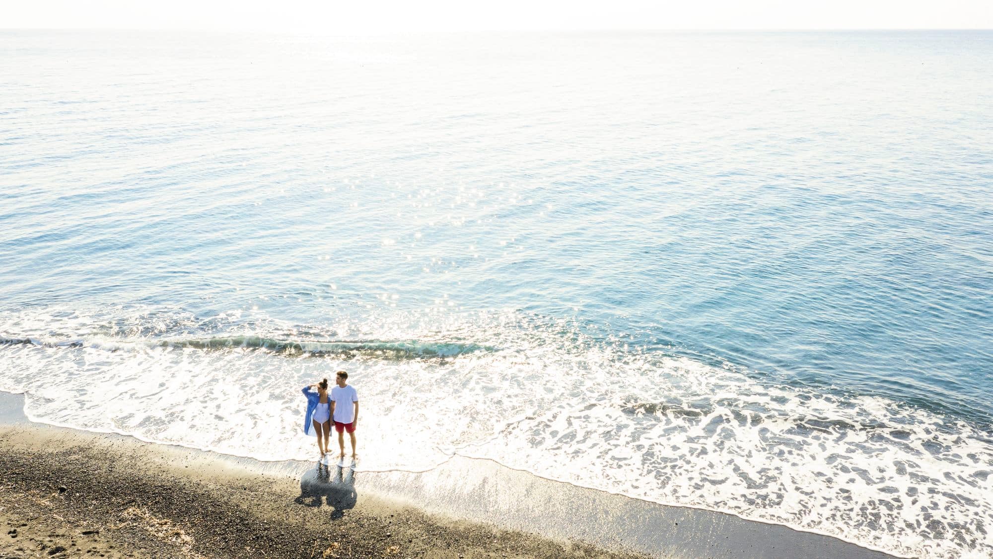 A couple standing by the sea and looking out towards the beach.
