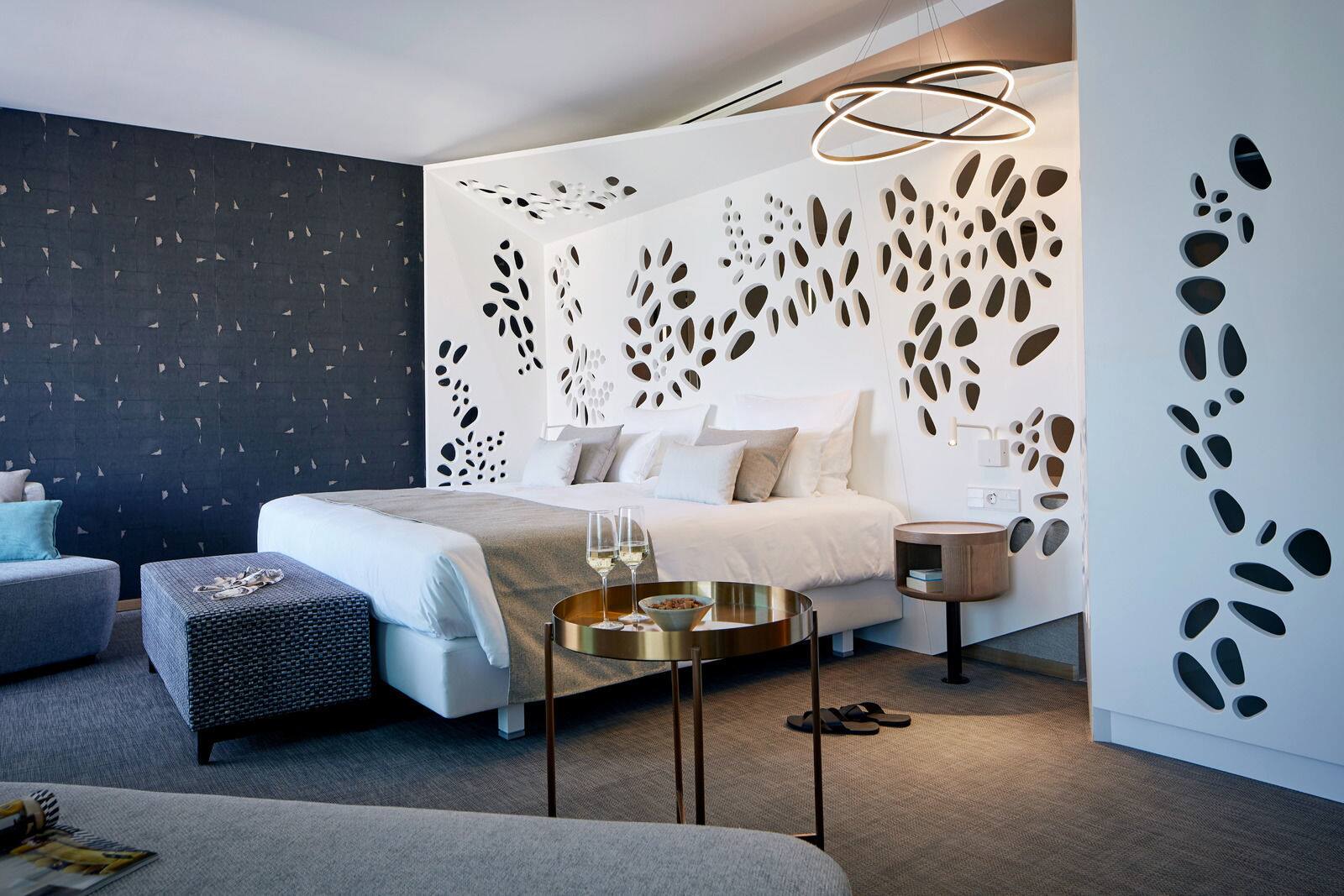 Luxury hotel room interior featuring a white platform bed with layered pillows against a striking white wall.