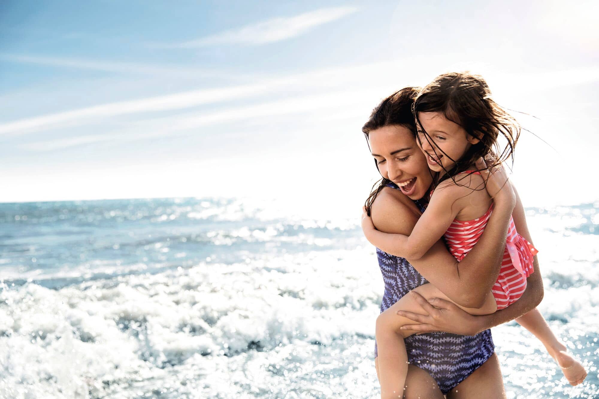A woman holding her child at the beach.