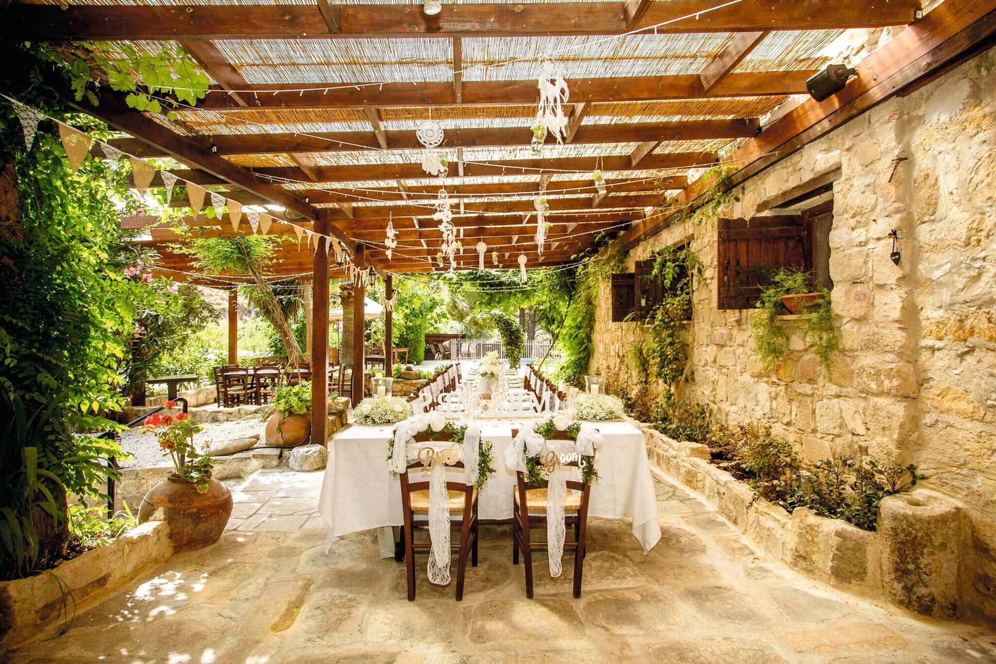 Wedding tables and chairs are set up on the terrace of a stone building.