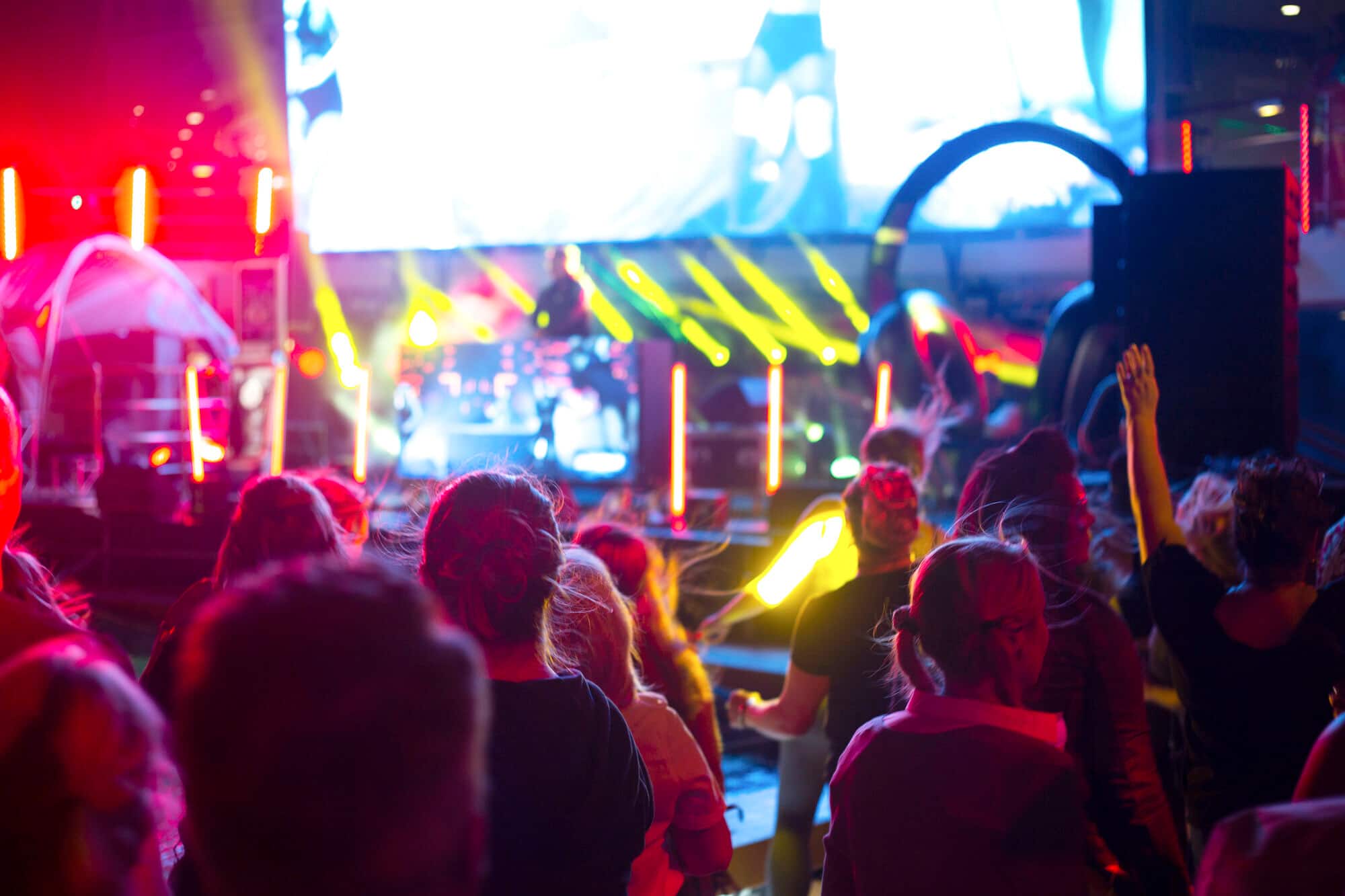 A crowd watching a neon-lit DJ set on the top deck of a Marella ship.
