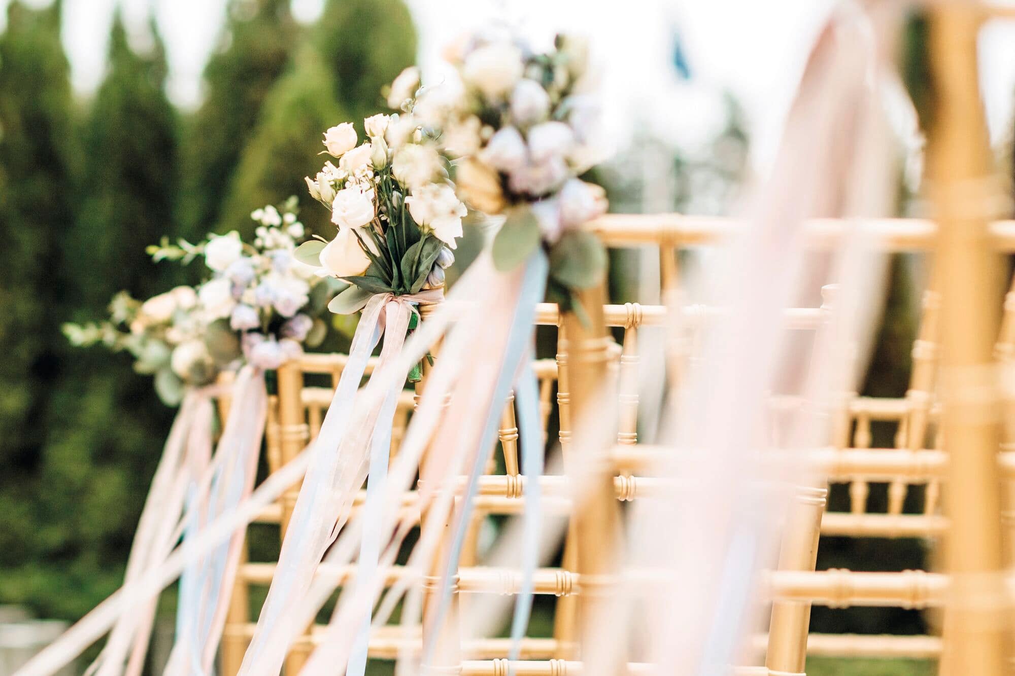 A close up of pretty flower arrangements and ribbons attached to chairs lining the aisle.