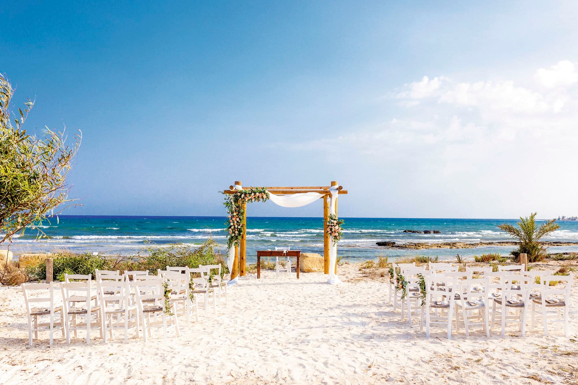 A wedding alter on a beach with white sand in front of the sea. 