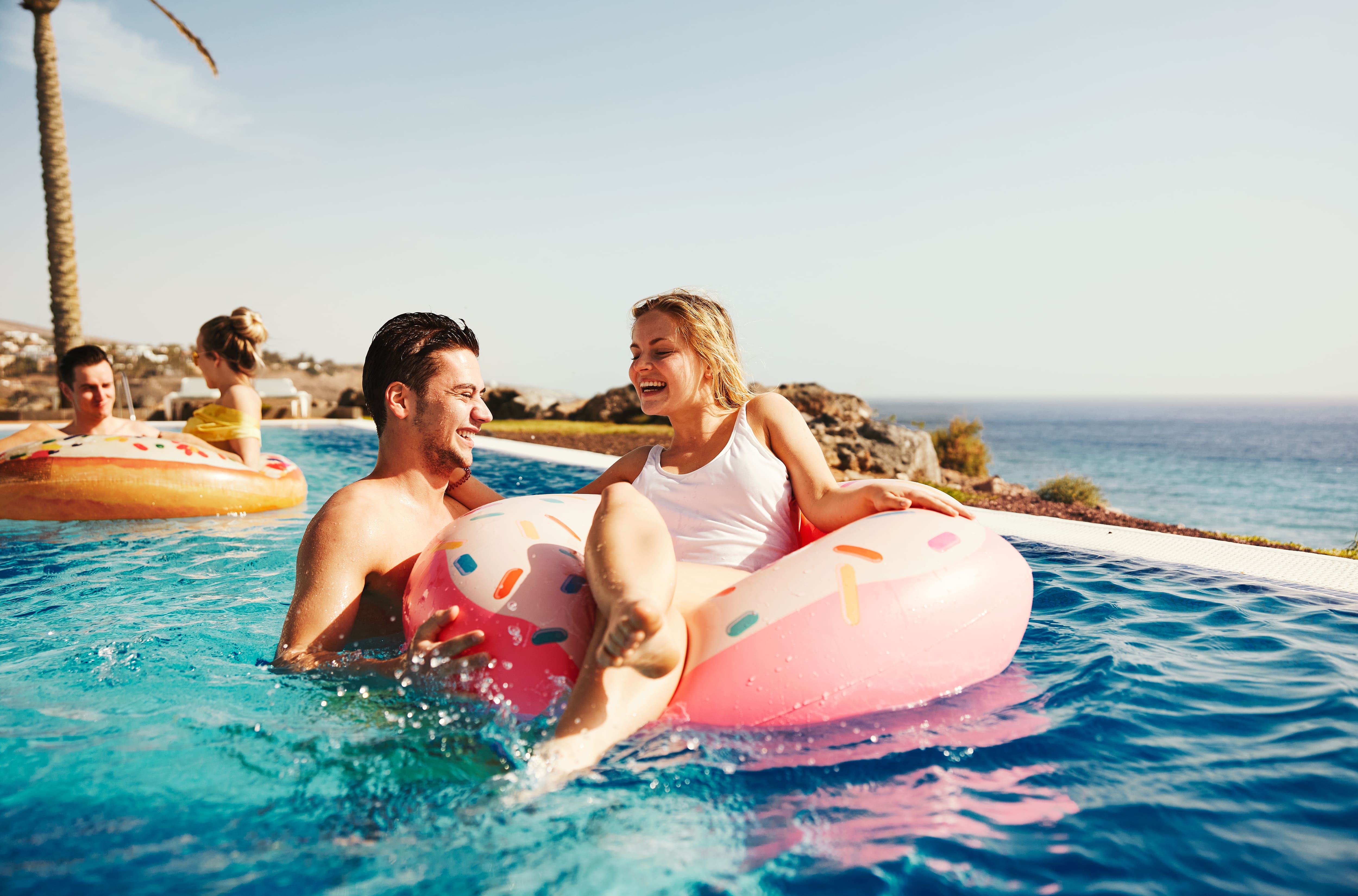 Happy couple on a flamingo float in a sunny resort pool.