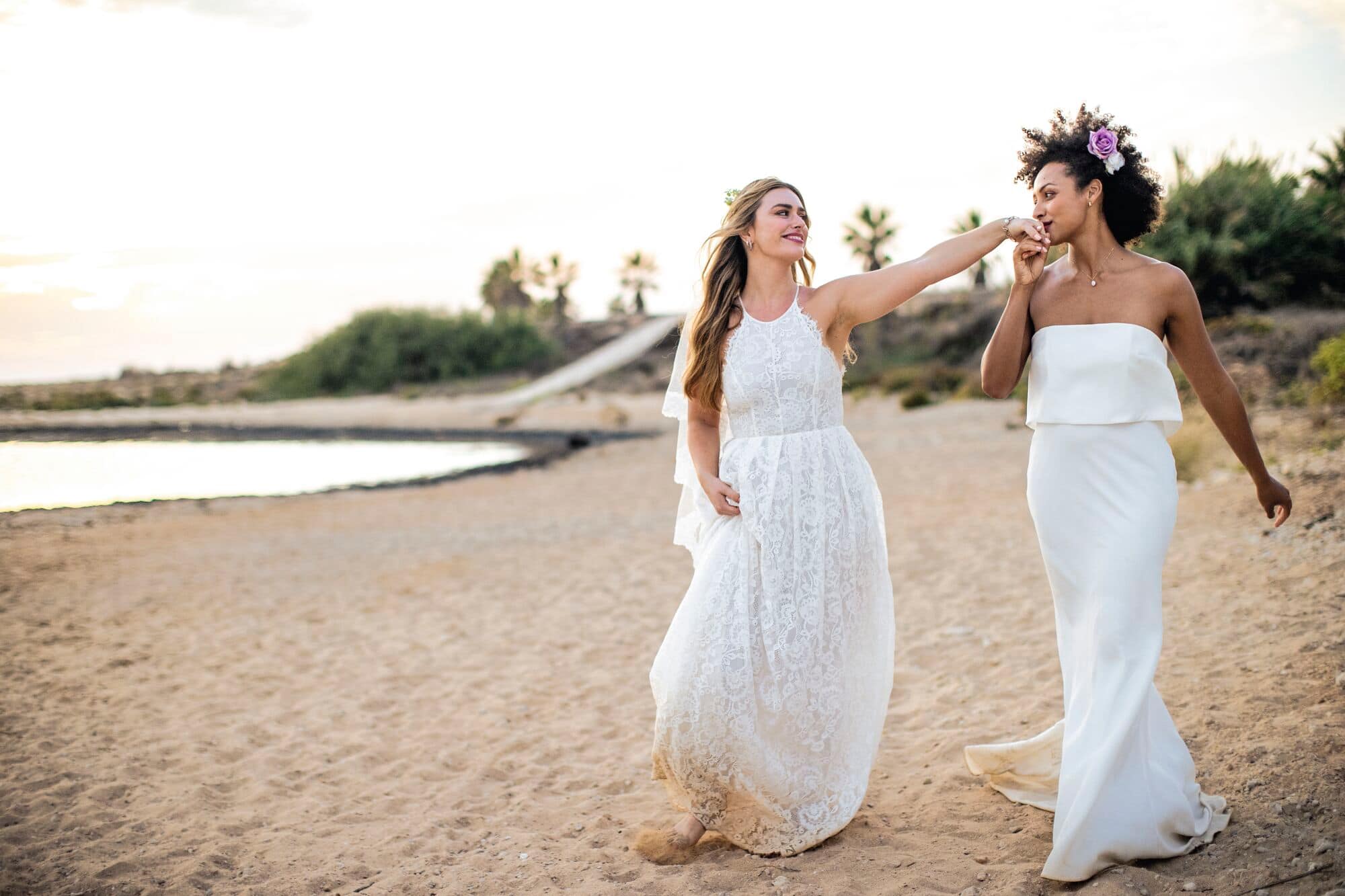 A same-sex newlywed couple walk along the beach.