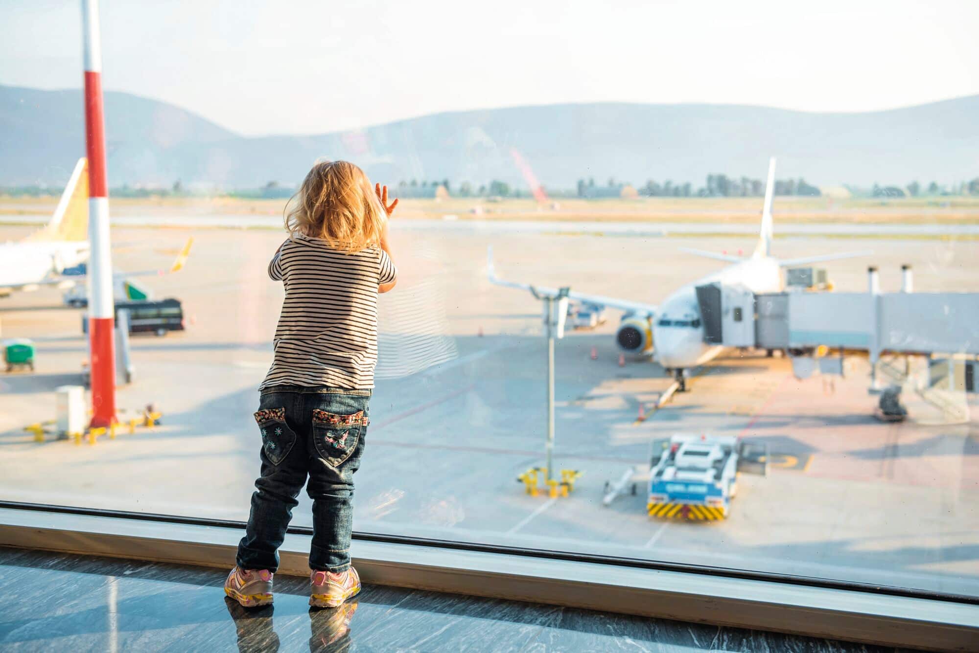 A view of little girl looking through an airport window at a plane.