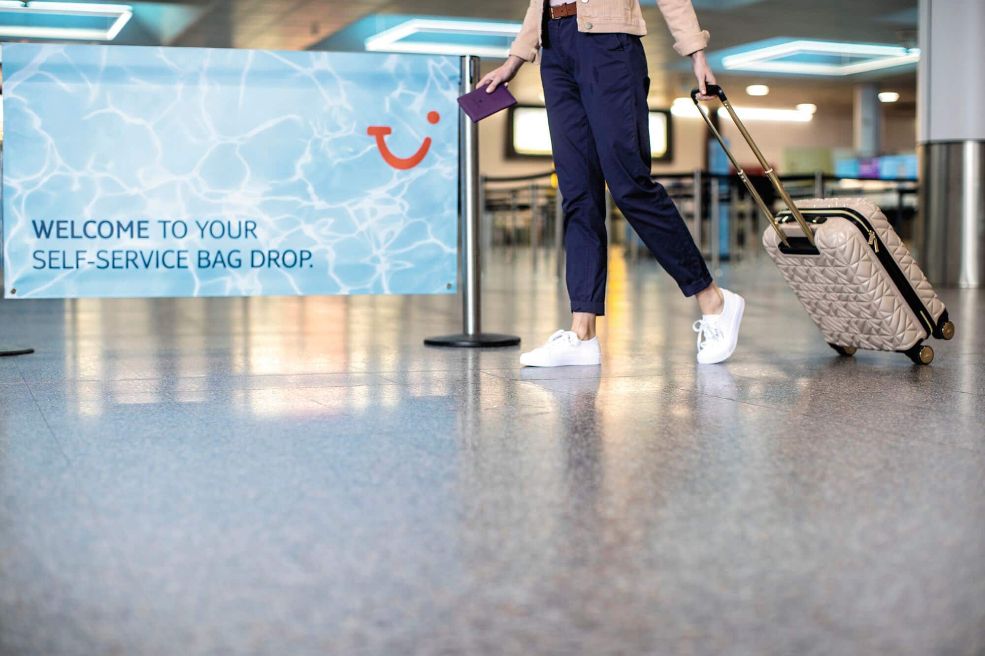 A close-up of a person with luggage in front of a self service bag drop sign.