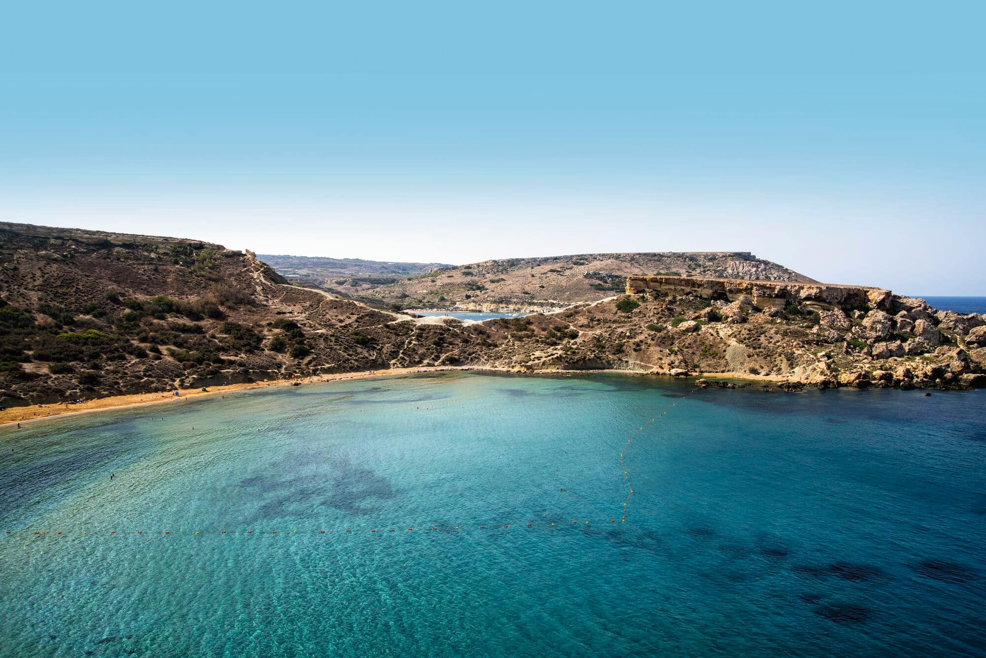 Aerial view of a secluded Mediterranean cove with crystal-clear water, surrounded by rocky hillsides.