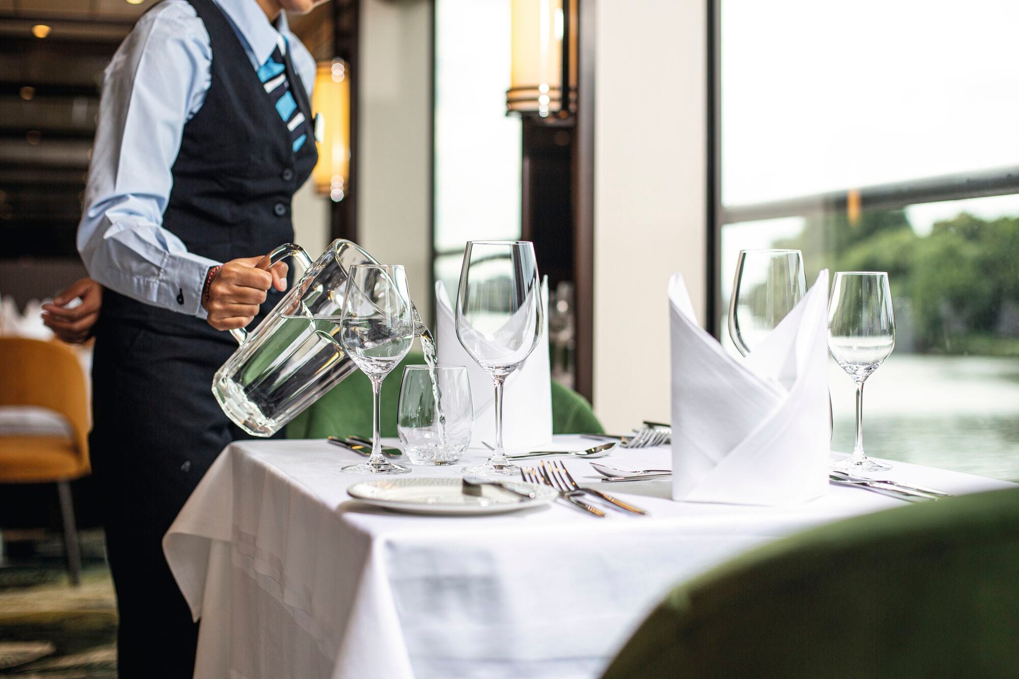A waiter pouring water into glasses at a dining table.