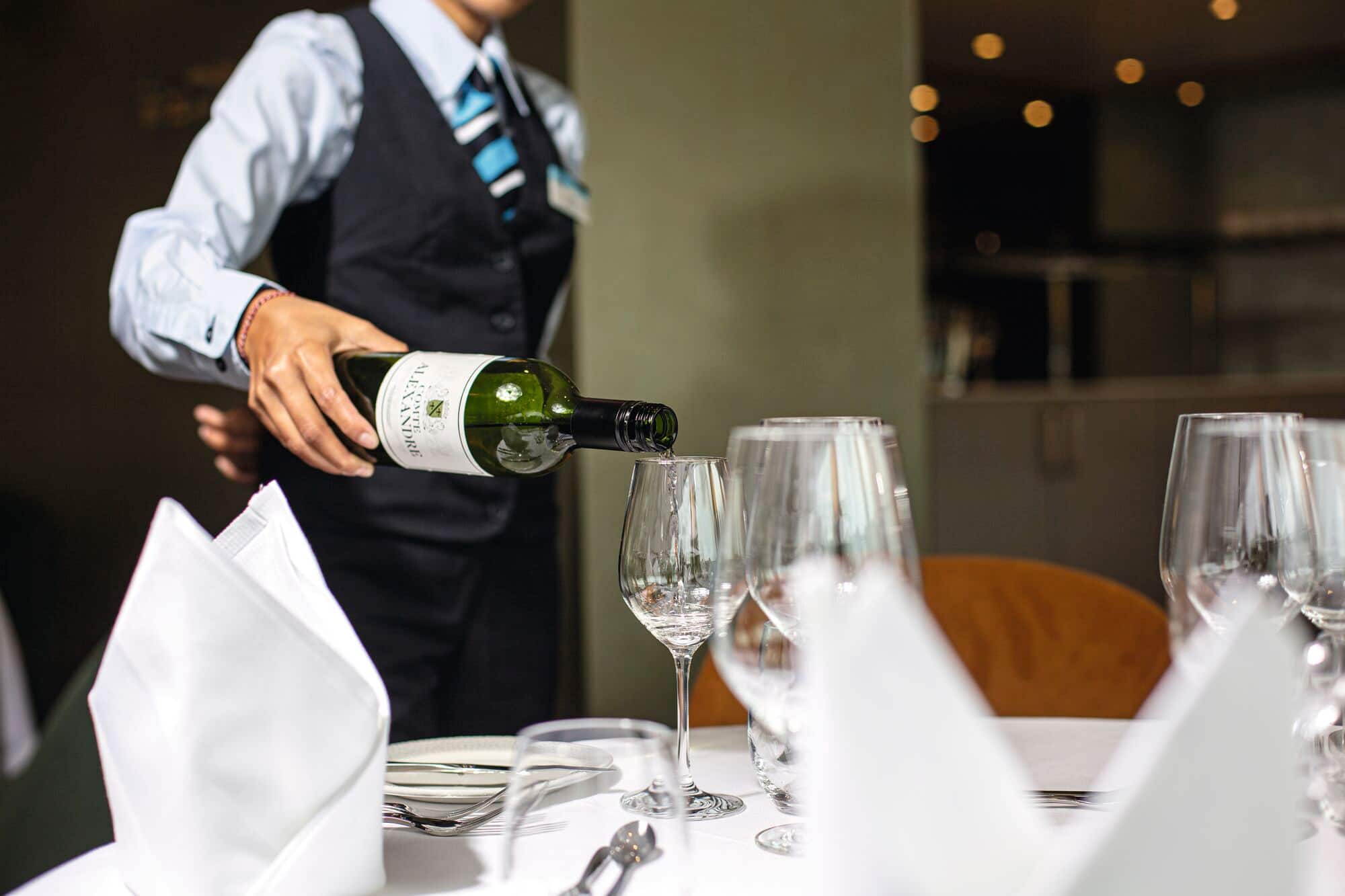 A Waiter pouring wine at a fine dining restaurant table.