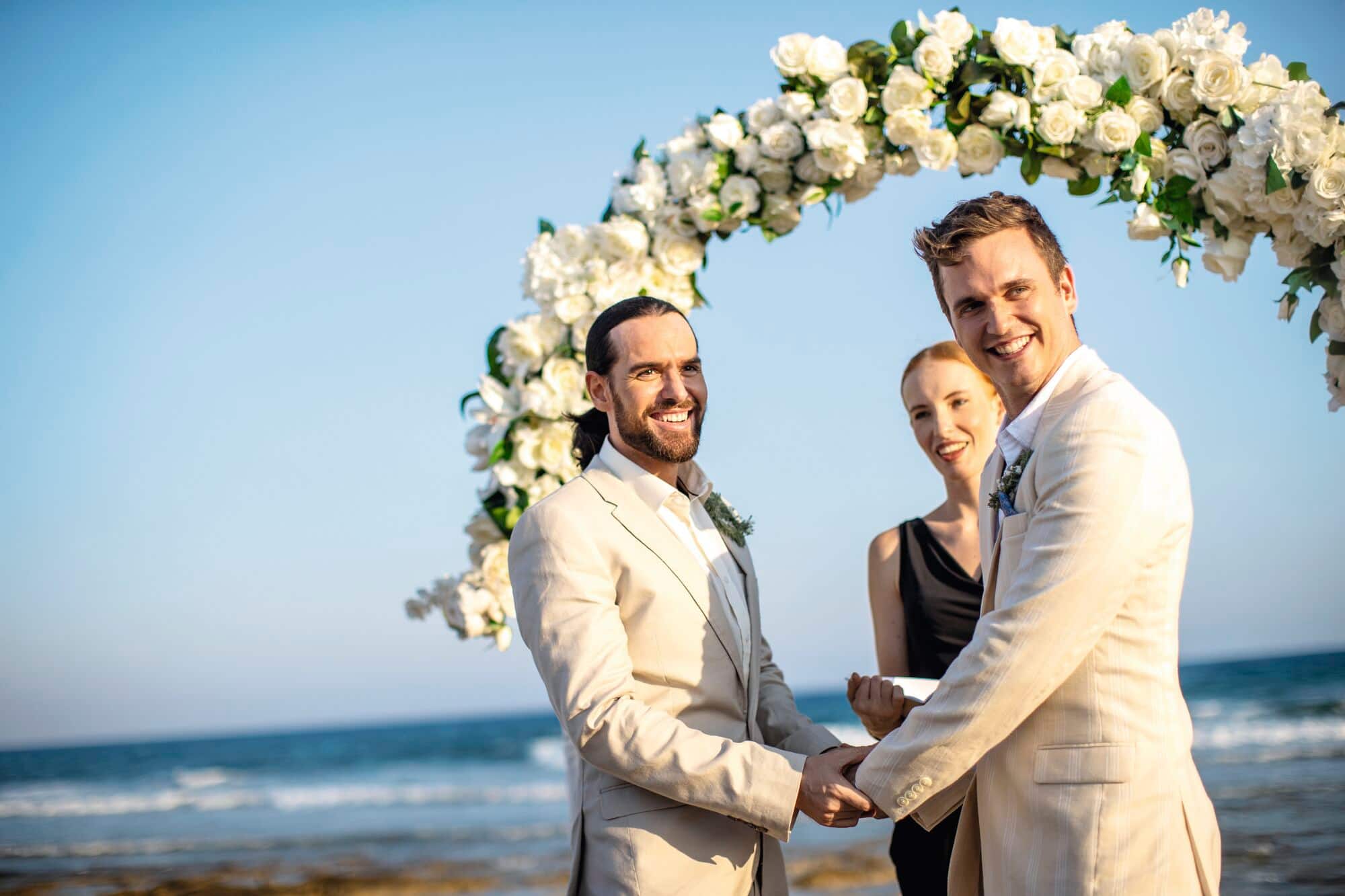 A same-sex couple smile whilst stood at the altar.