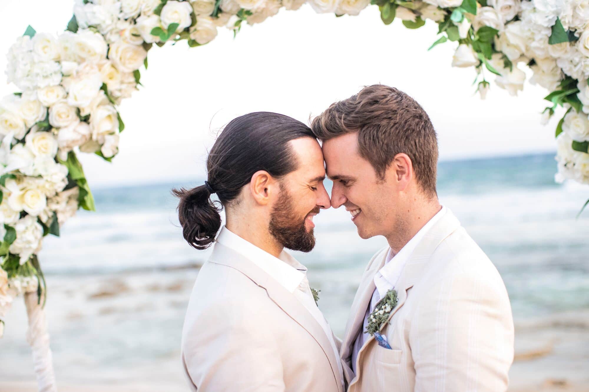 A same-sex couple stand under a floral arch.