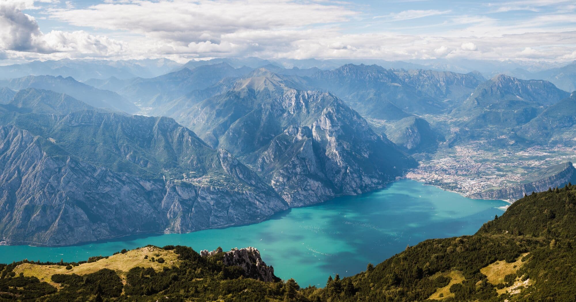 A blue lake surrouded by mountains with a town at one end, seen from above. 