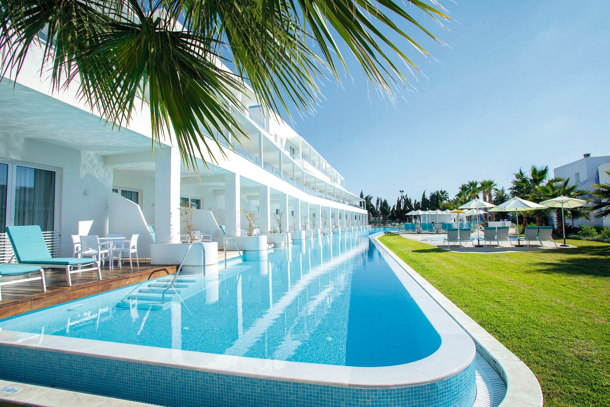 A long shared swim-up pool in front of a row of hotel room terraces.