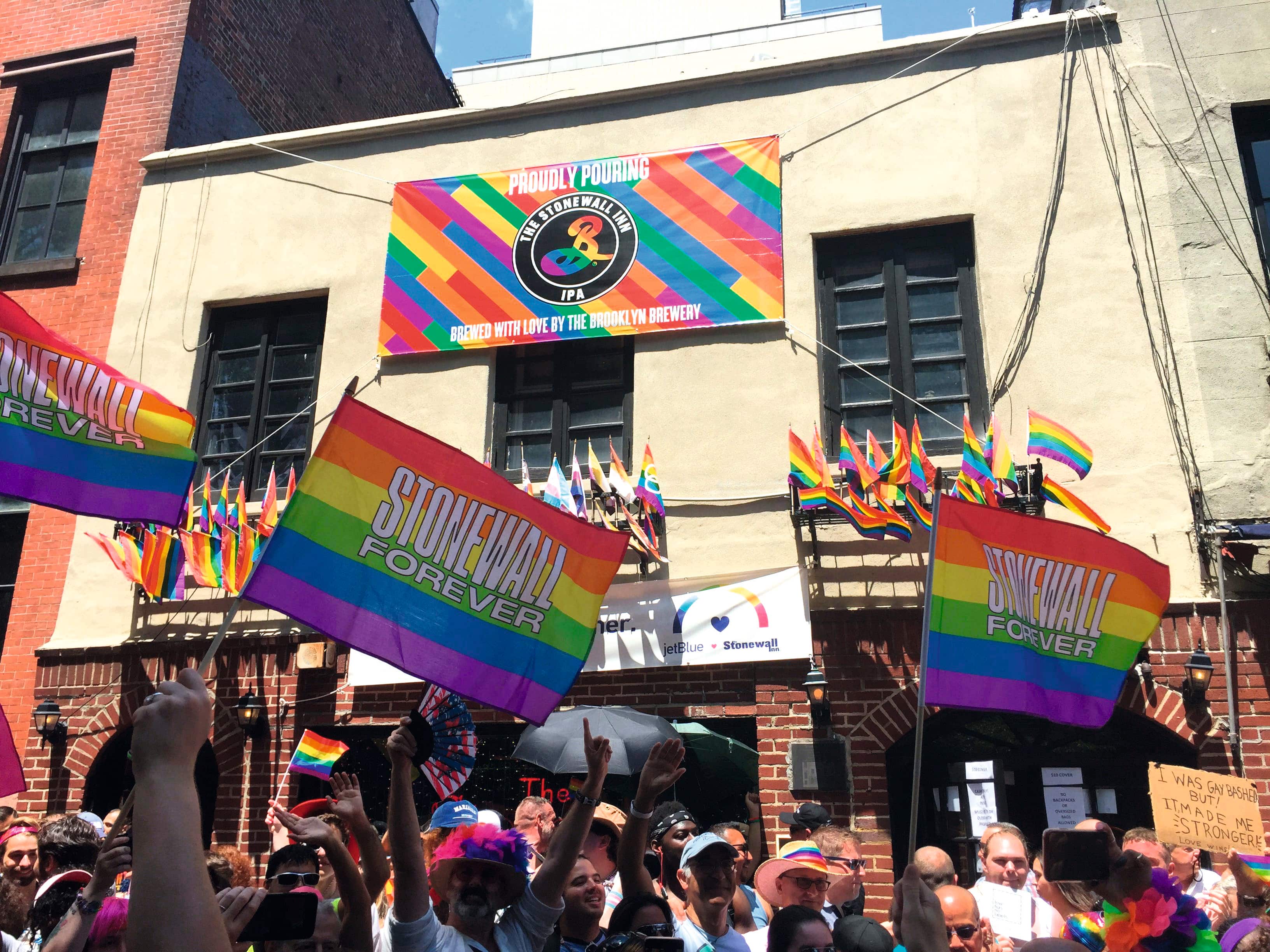 The historic Stonewall Inn building with cream-colored facade decorated with rainbow Pride flags reading 'STONEWALL FOREVER' and a large banner.