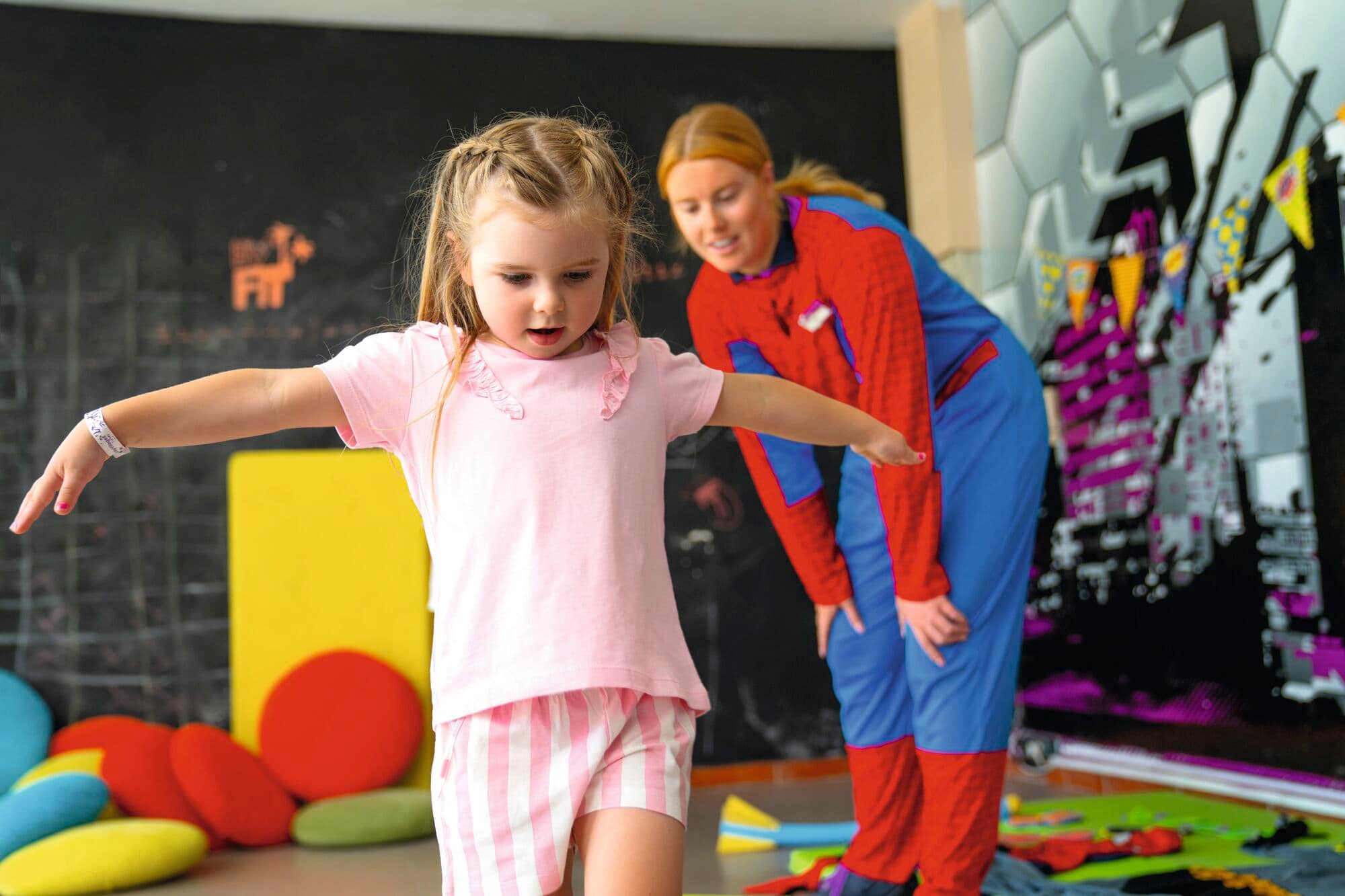A toddler in front of a kids' club staff member dressed in a Spider-Man costume.
