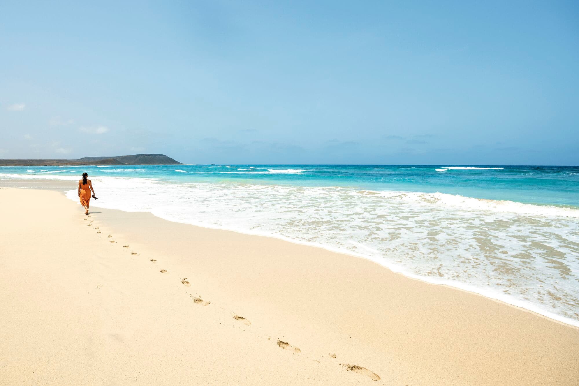 A person walking alone along a sandy beach, leaving footprints behind.