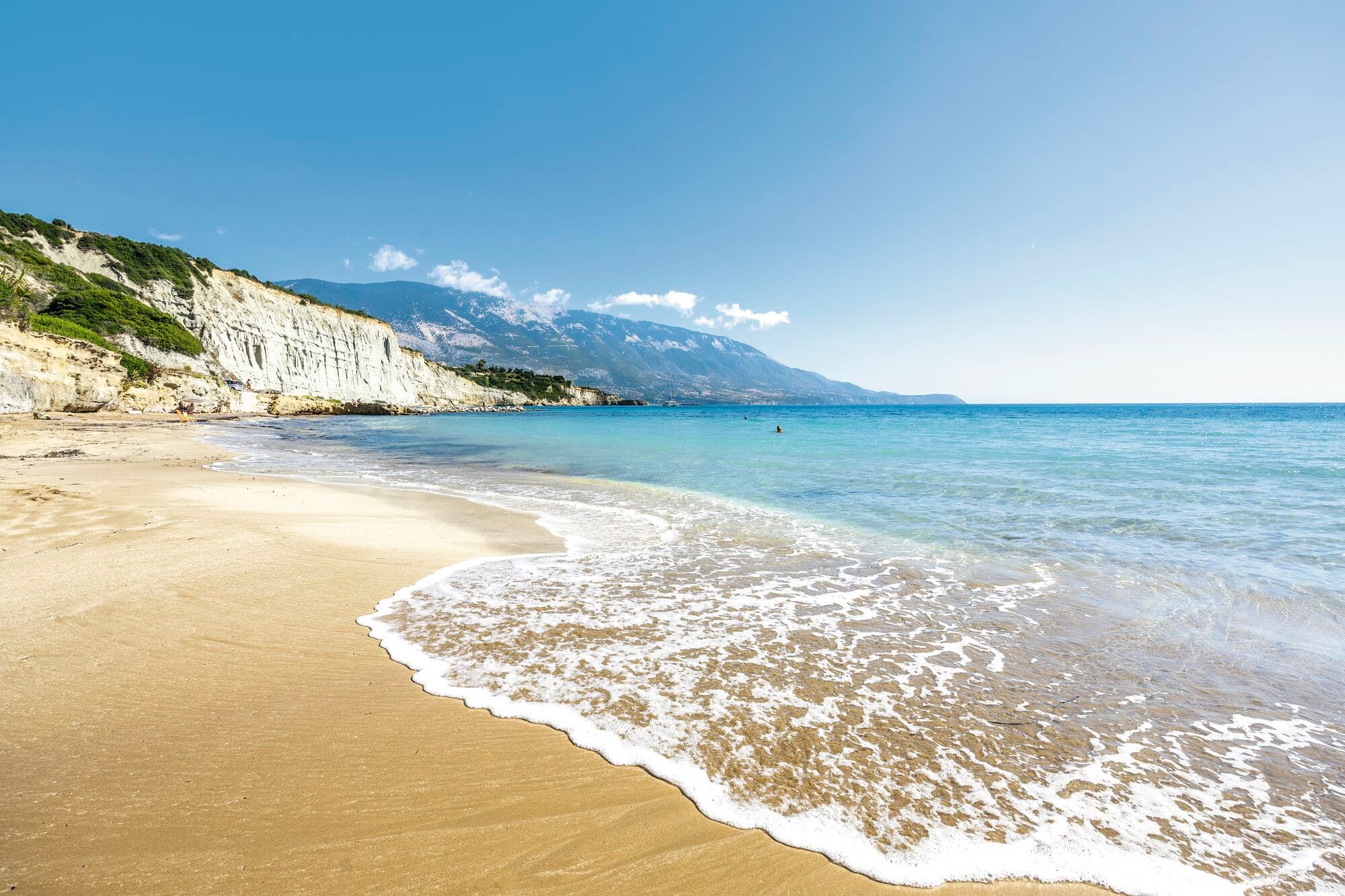 A golden sandy beach on the coast of Kefalonia, with white limestone cliffs stretching into the distance. 