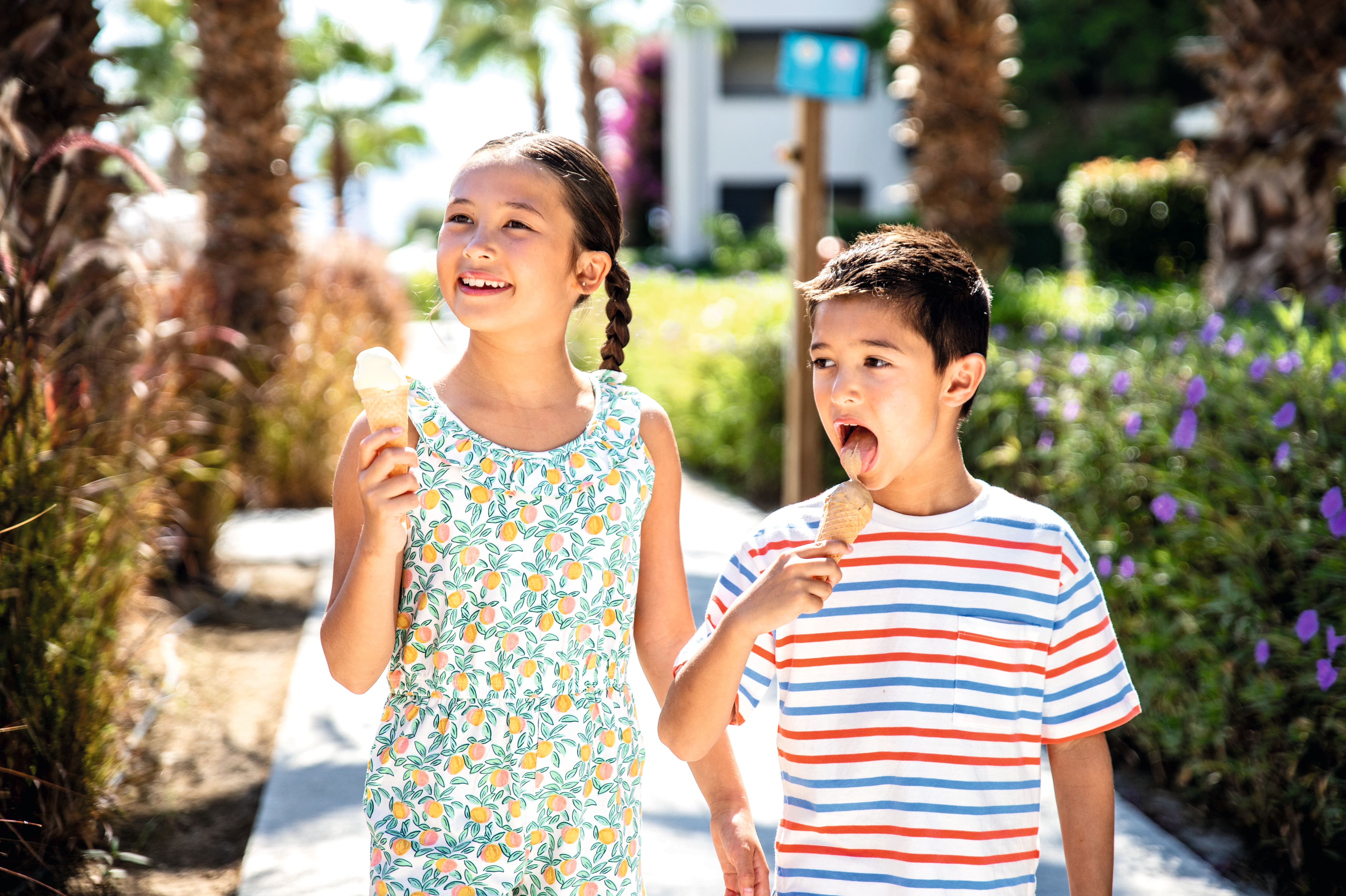 Two children eating ice-cream in front of hotel gardens.