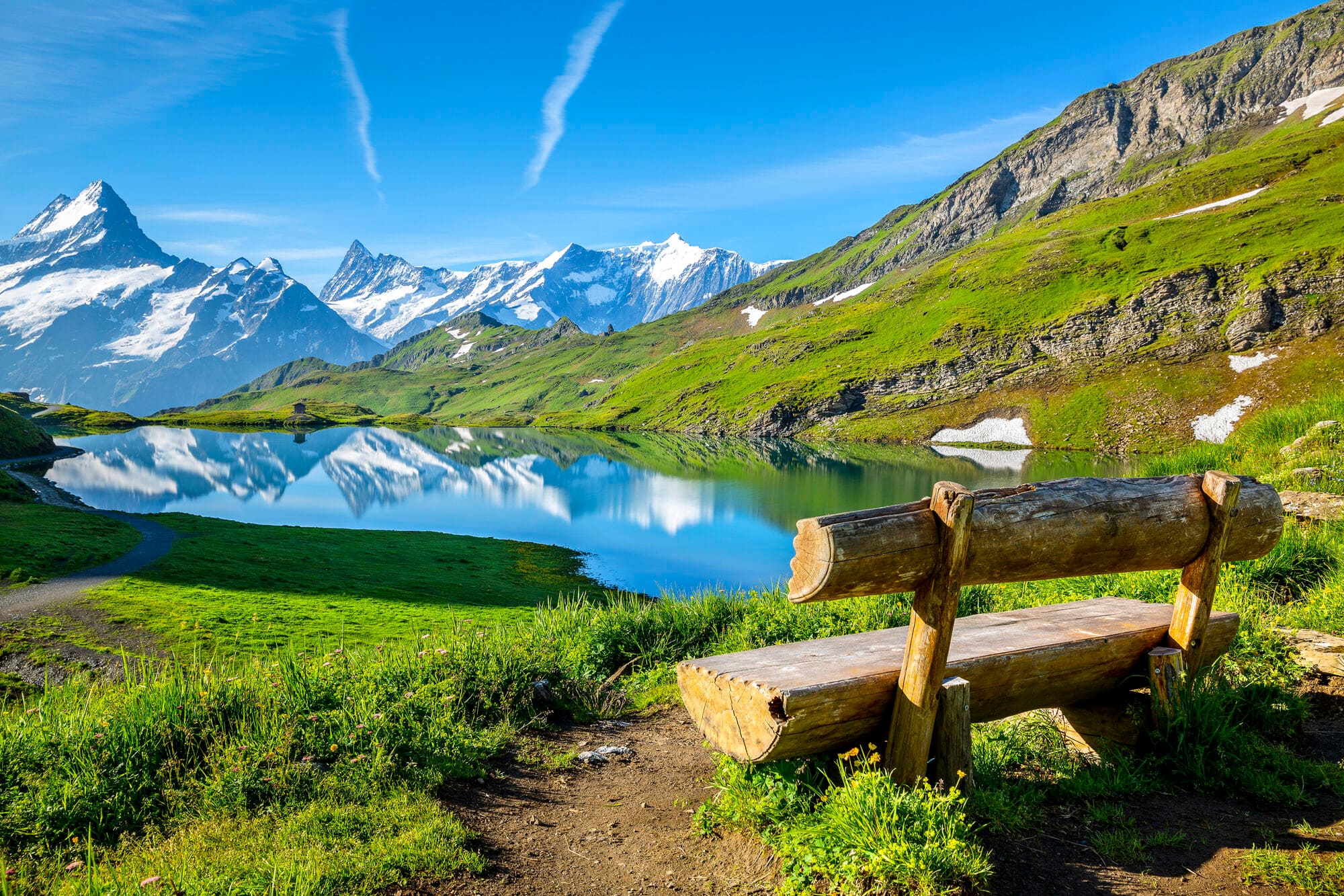 A wooden bench beside a blue lake in Switzerland with mountains beyond.