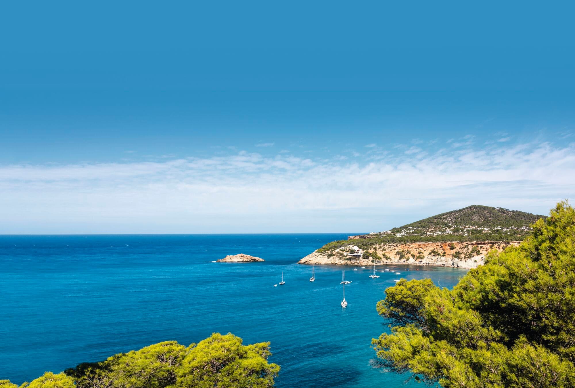 Mediterranean coastal view with turquoise waters, scattered white sailboats in a bay.