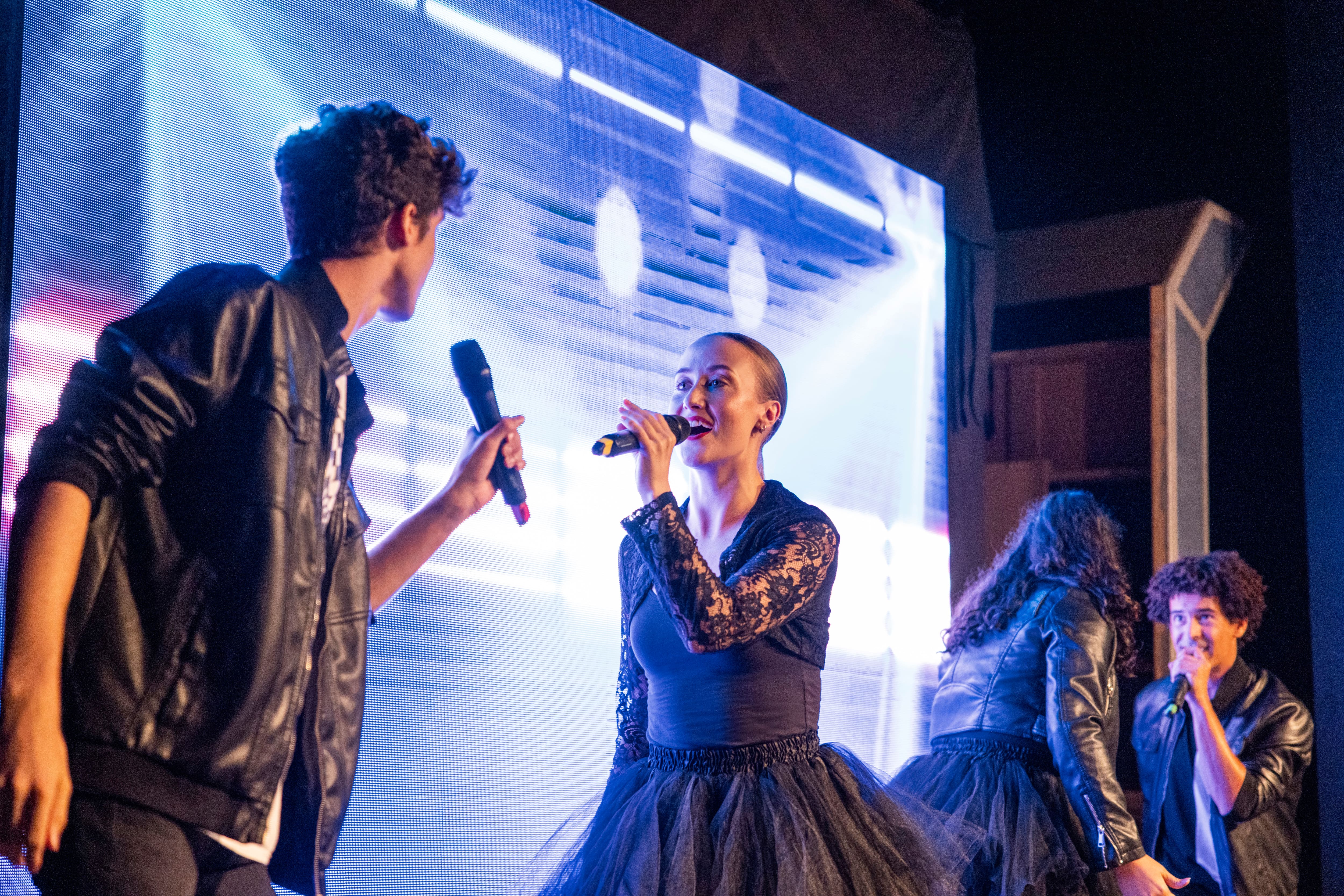 Four performers dressed in black and singing on stage.