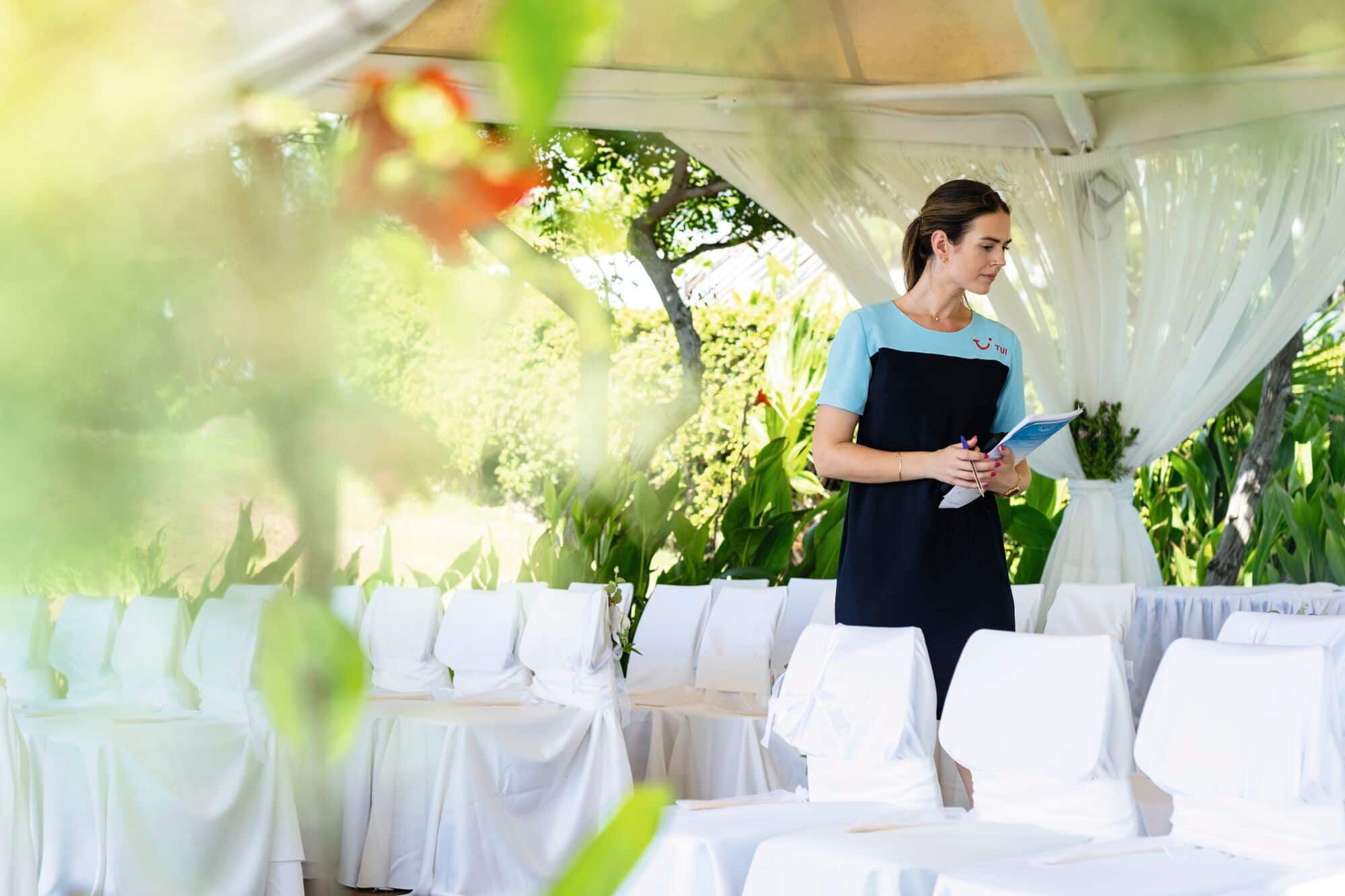 A TUI event co-ordinator in blue uniform inspects a wedding ceremony set-up.