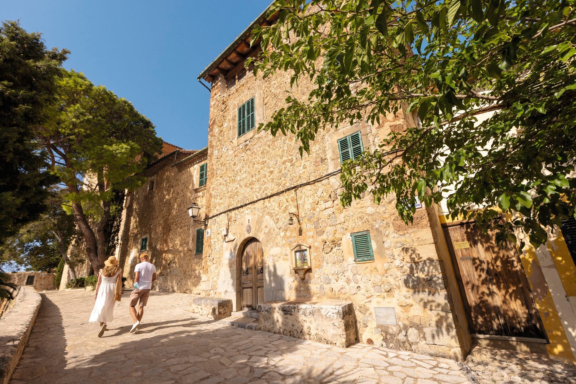 A couple walking along a cobblestone street lined with rustic stone buildings.