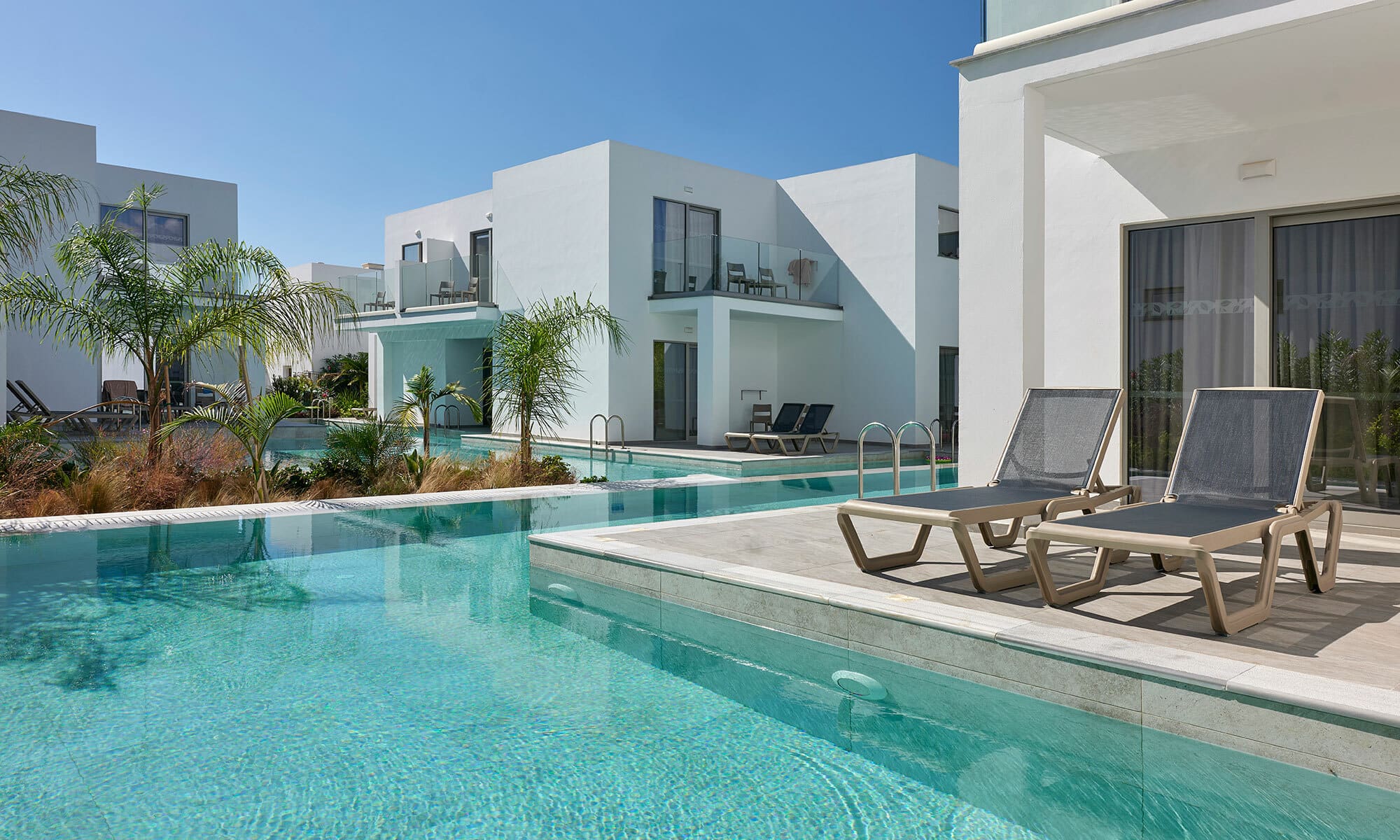 Two sunbeds beside a swimming pool outside a hotel room
