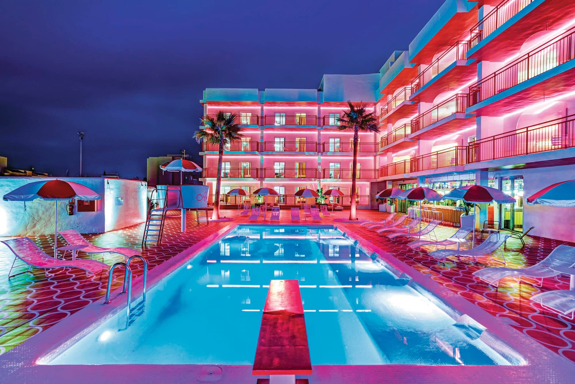 An outdoor pool lit up in pink and blue hues at night.