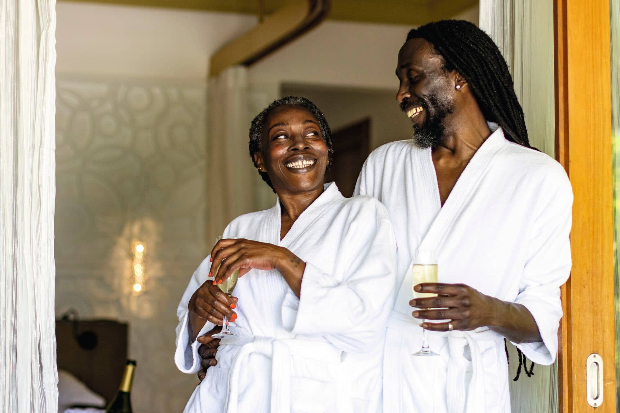 A couple in white bathrobes embracing and celebrating with champagne in luxury hotel    