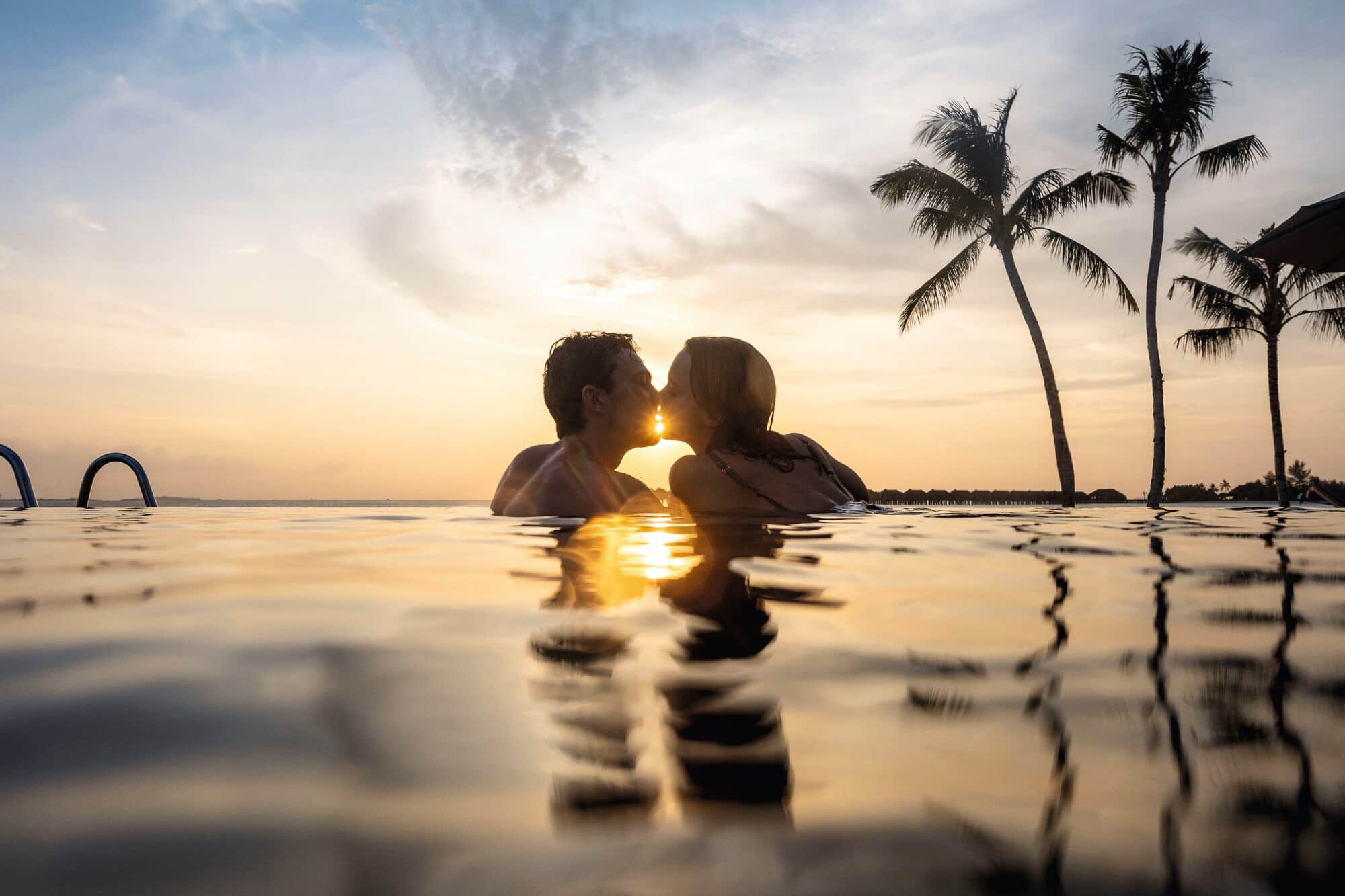 A silhouetted couple kissing in an infinity pool at sunset.