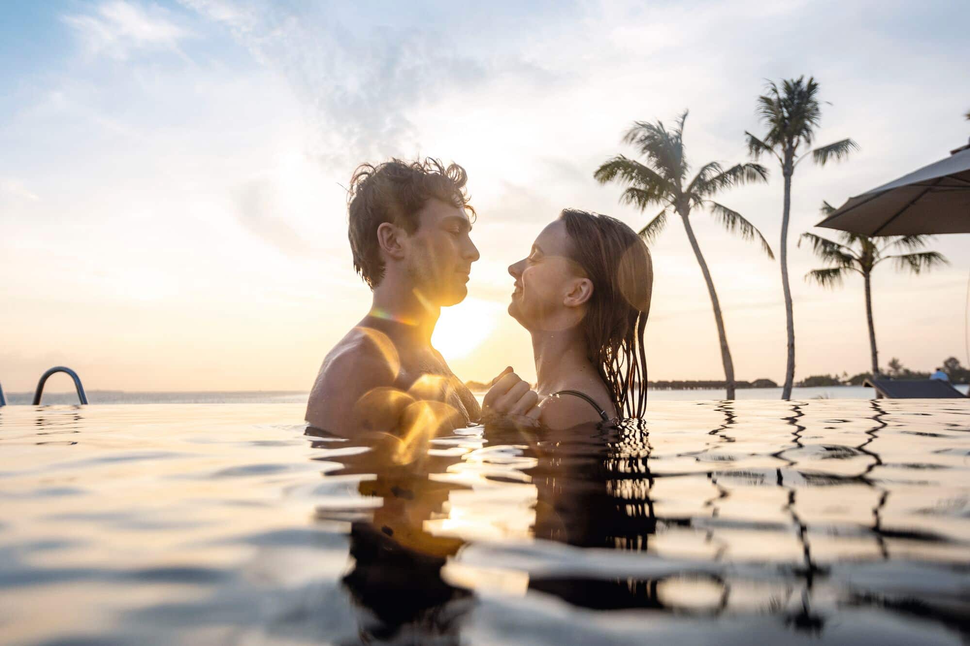 A couple in a swimming pool at sunset.