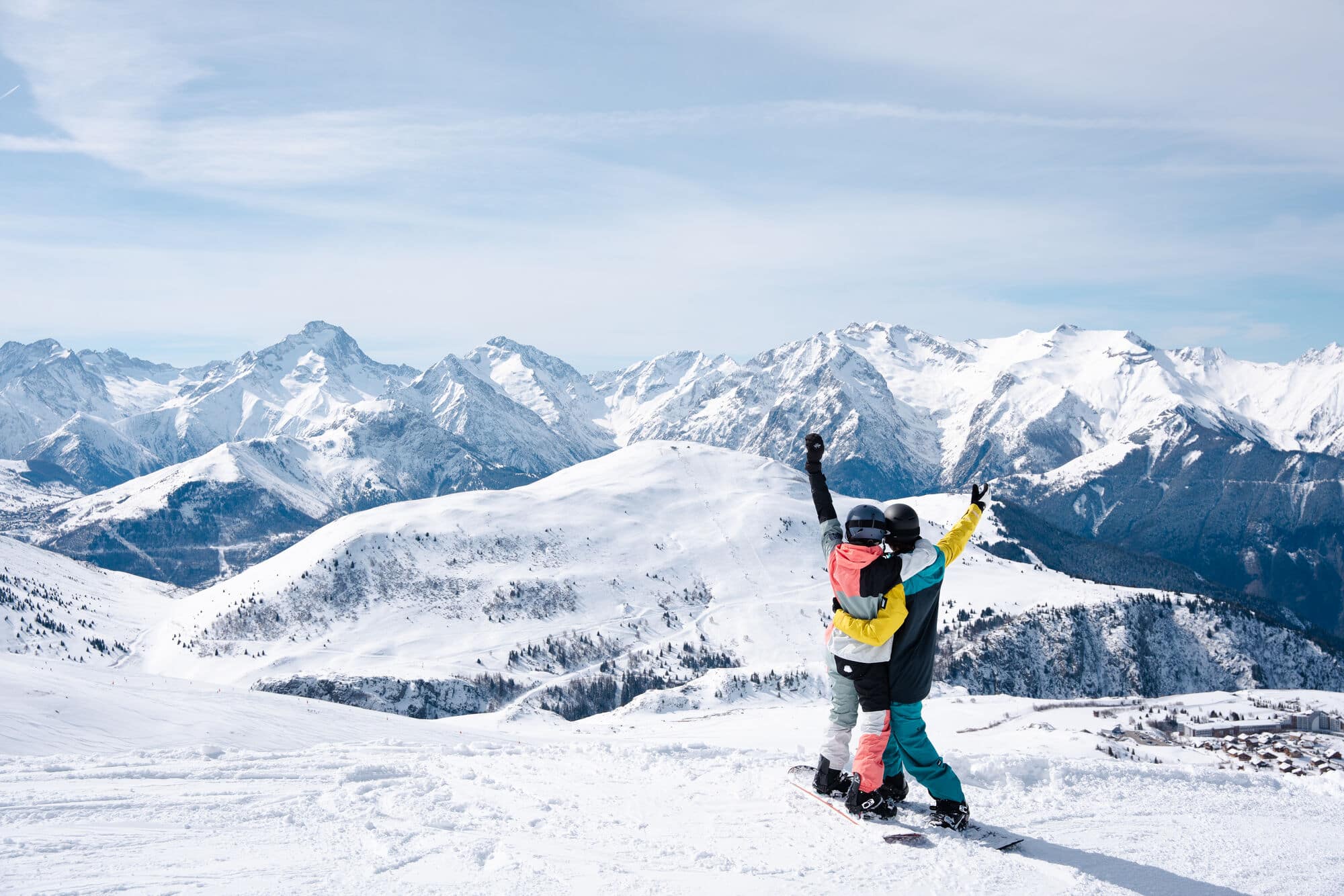 Two people looking out over a mountain view with their arms in the air.