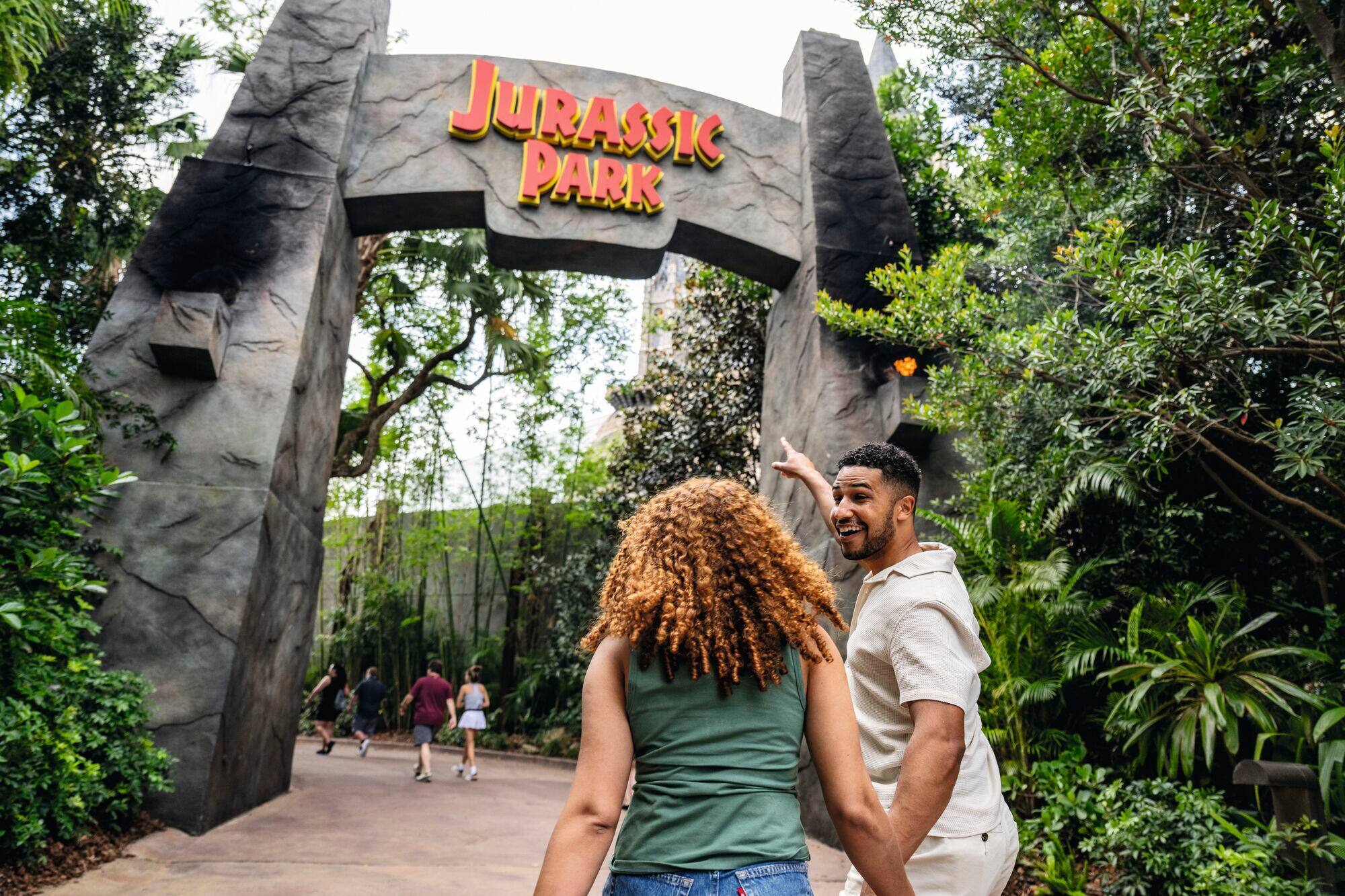 Couple walking toward Jurassic Park arch, surrounded by greenery – adventure starts here.